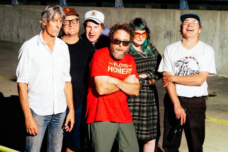 Six people in casual wear stand in a line in a concrete and asphalt structure at night