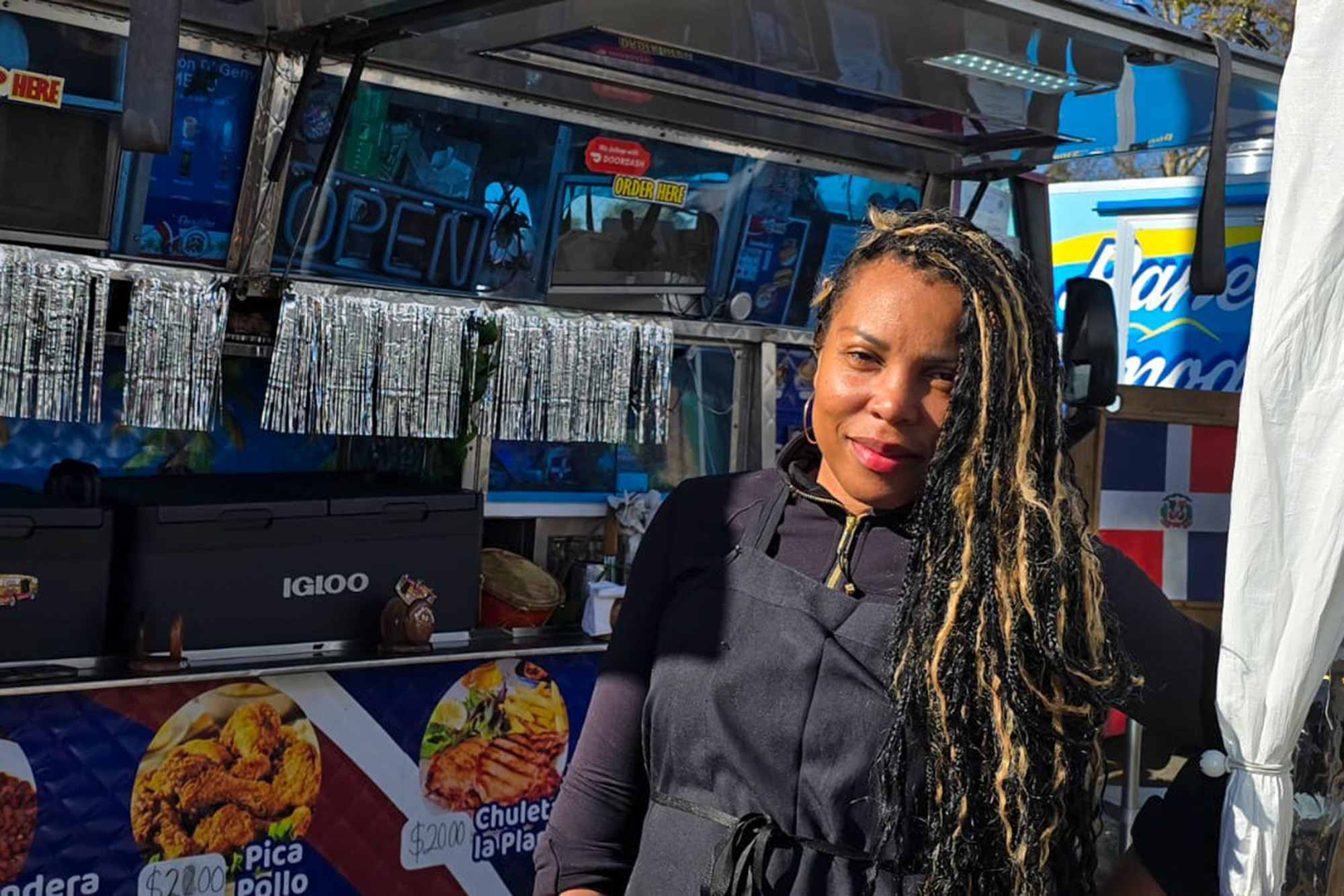 A woman with long braids poses for a portrait in front on her food truck.
