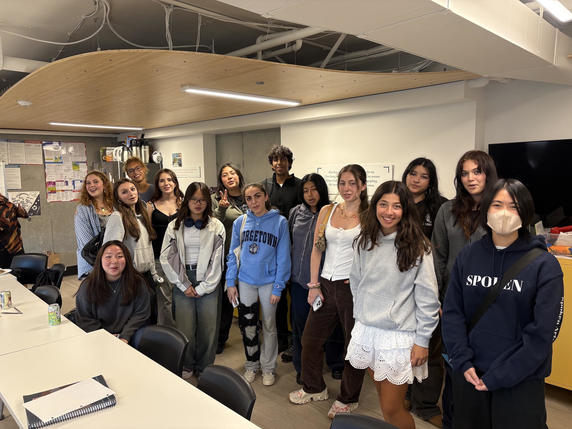 15 diverse teenagers stand in a classroom, smiling for the camera.