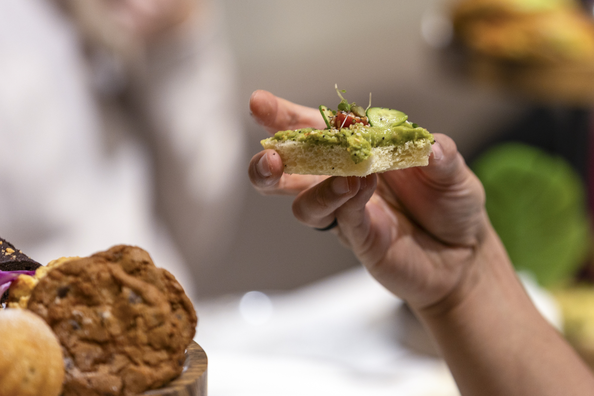 Close-up of a diner's hand holding up an open-face avocado sandwich.
