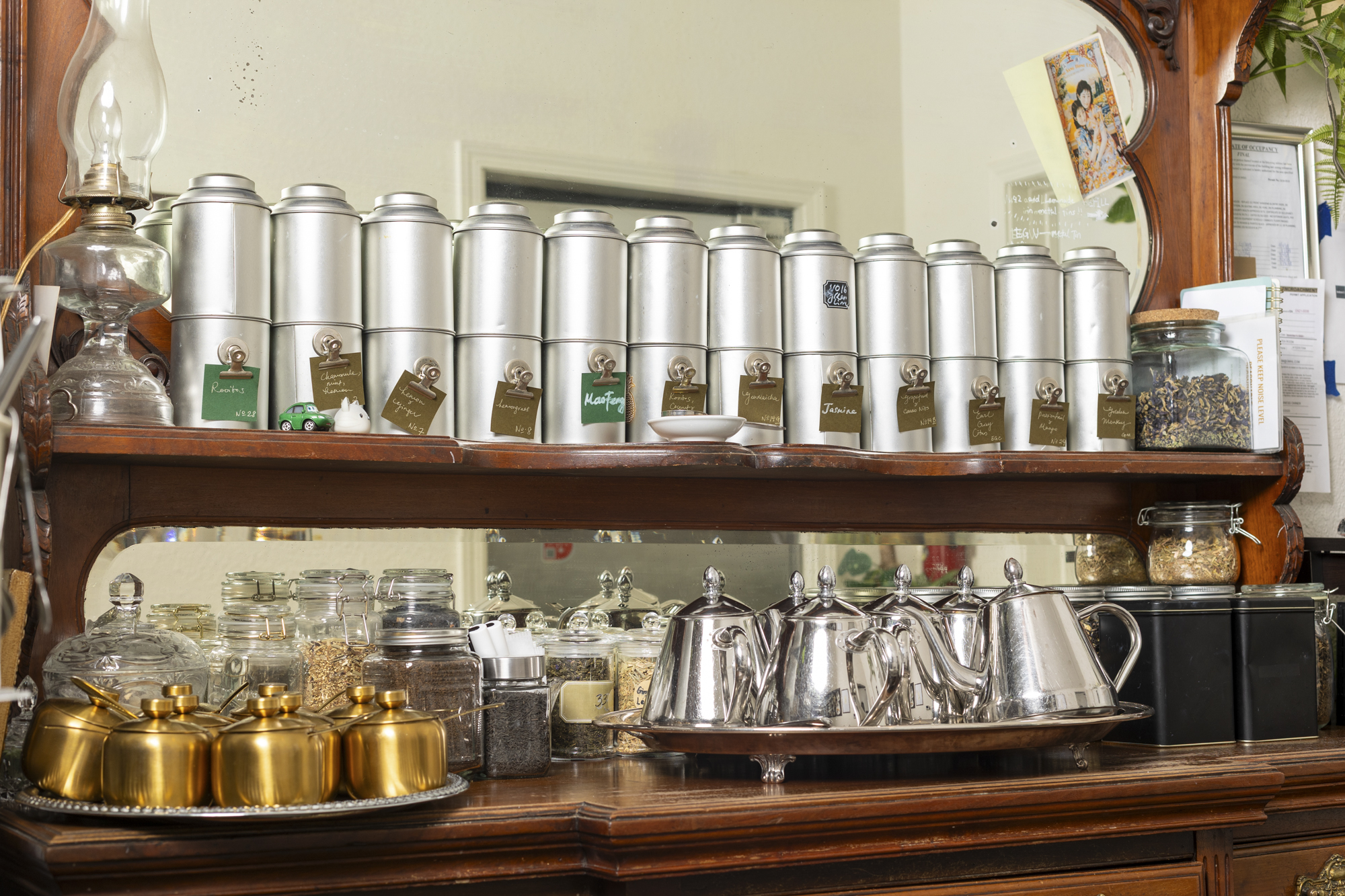 Tea kettles, sugar bowls and metal canisters of loose-leaf tea on a wooden credenza.