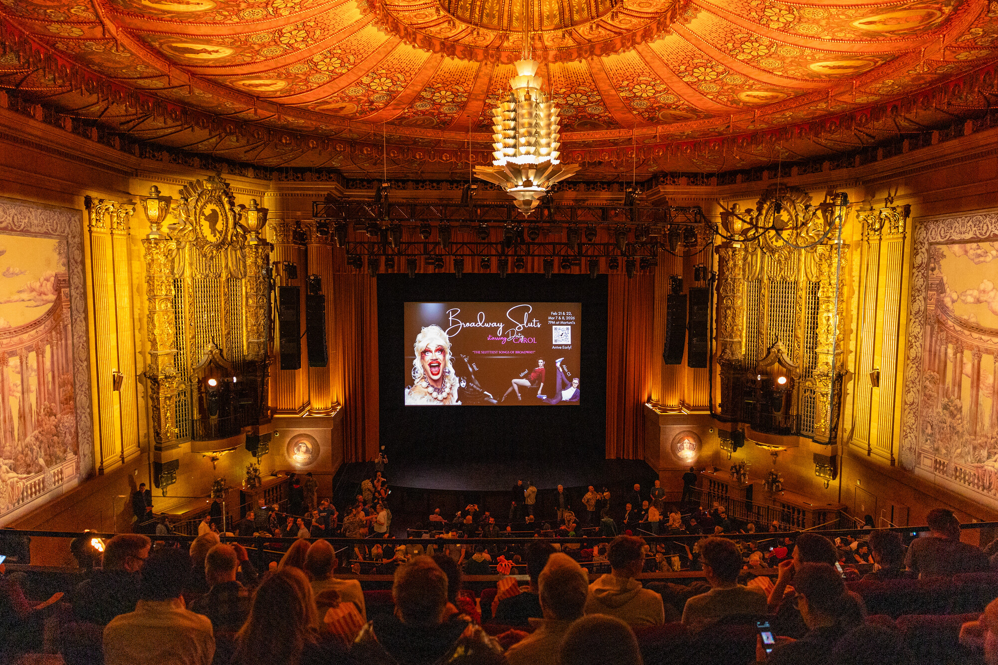 A panoramic view of an ornate 1920s movie theater, with a large ceiling in hues of yellow and orange