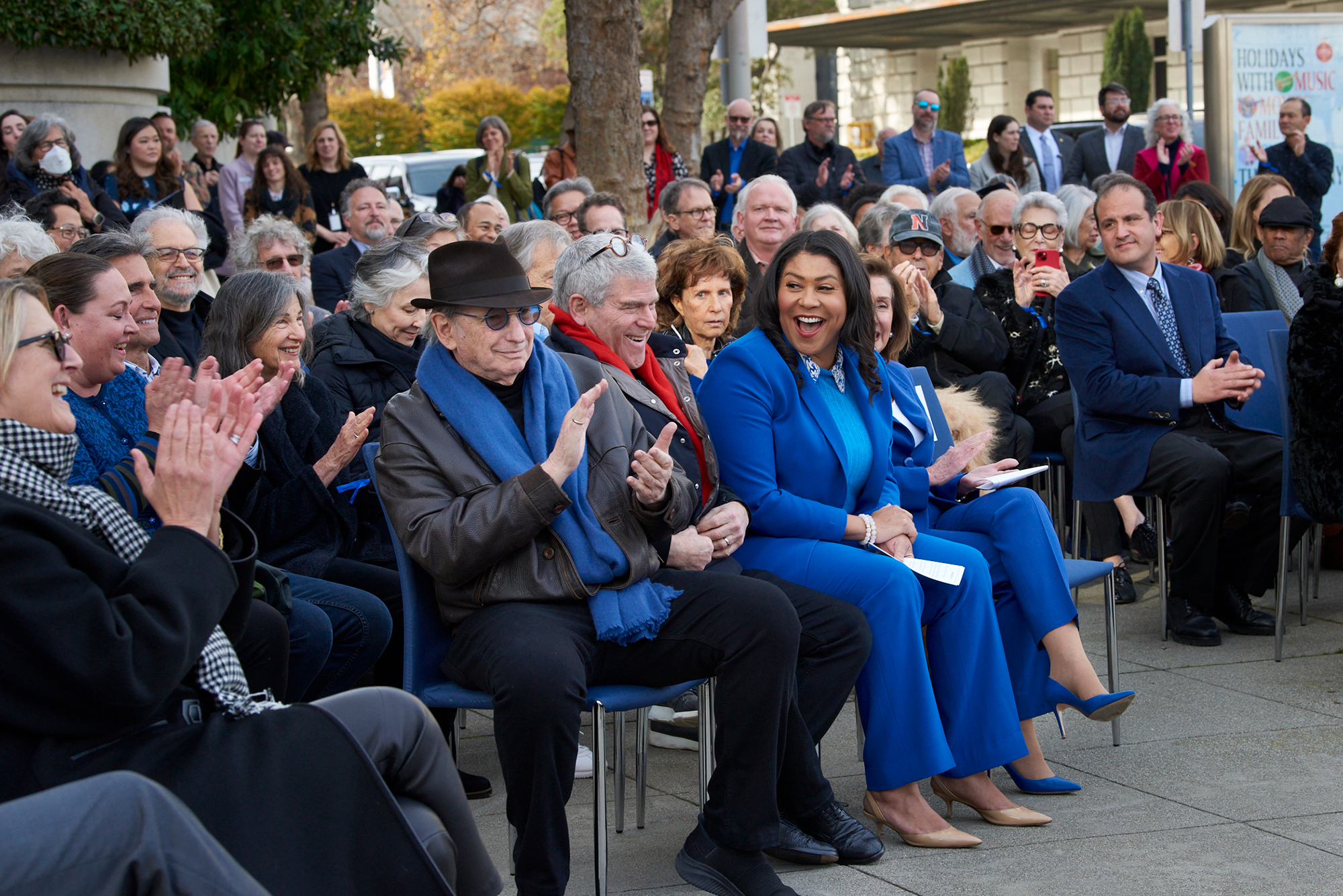 A group of people sit in chairs, many dressed in blue, on the sidewalk