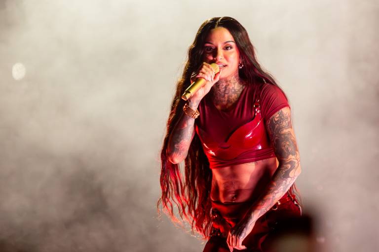 performer with long hair in red outfit holds mic against backdrop of haze