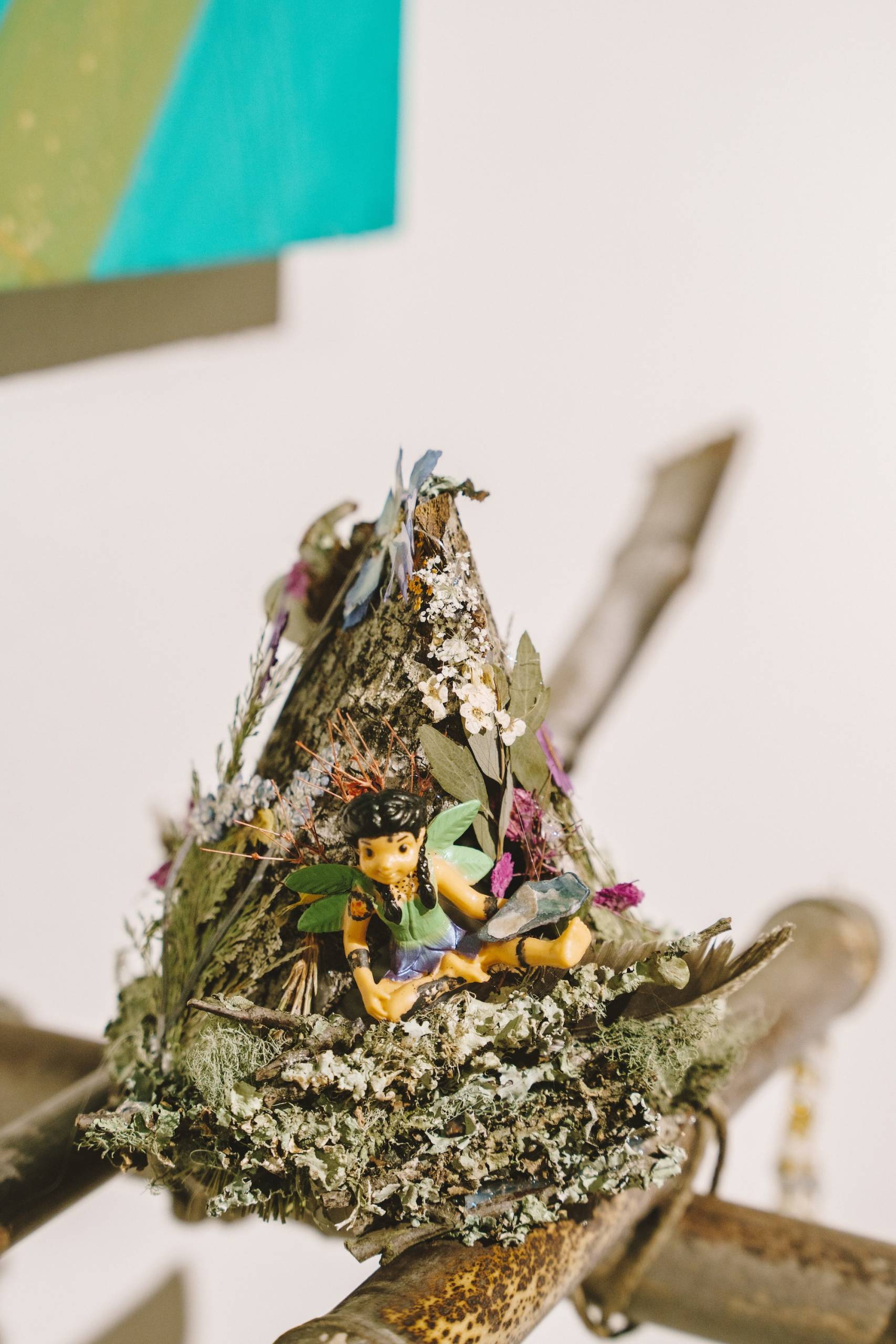 A small figurine placed in a pile of foliage, mounted on a bamboo-raft like object. 