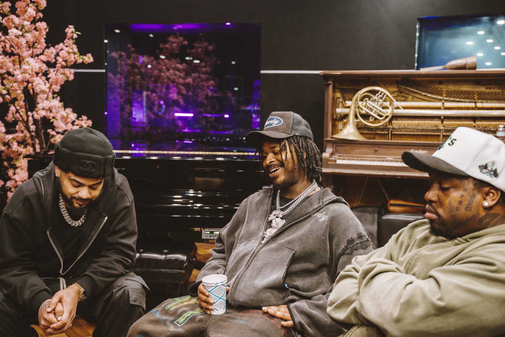 Three African-American men sit in a music studio while being interviewed.