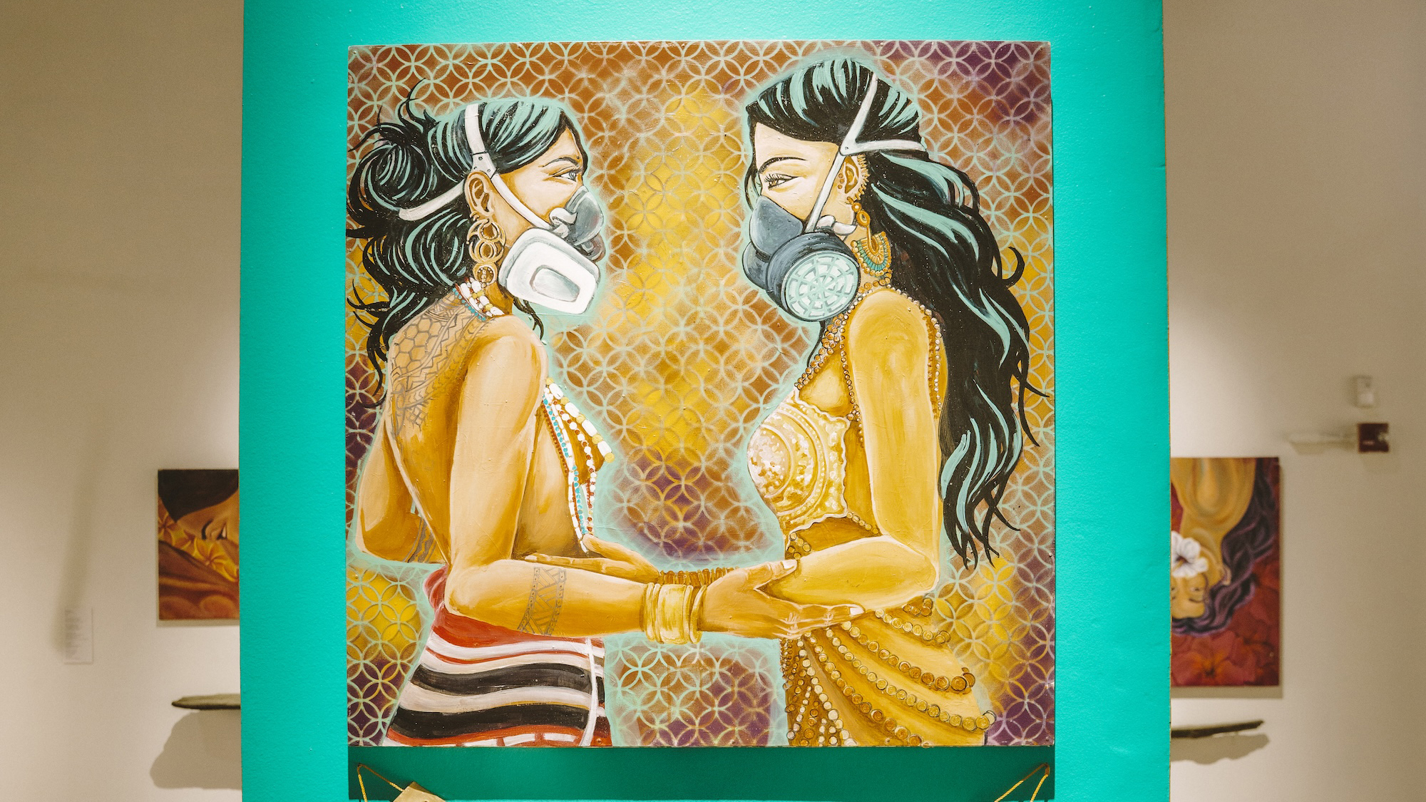 A painting of two women wearing masks, facing each other, mounted on a green background in an art gallery.