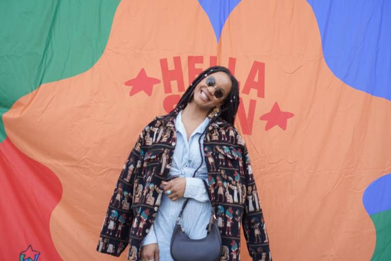 A Black woman with braids poses in front of a colorful background.