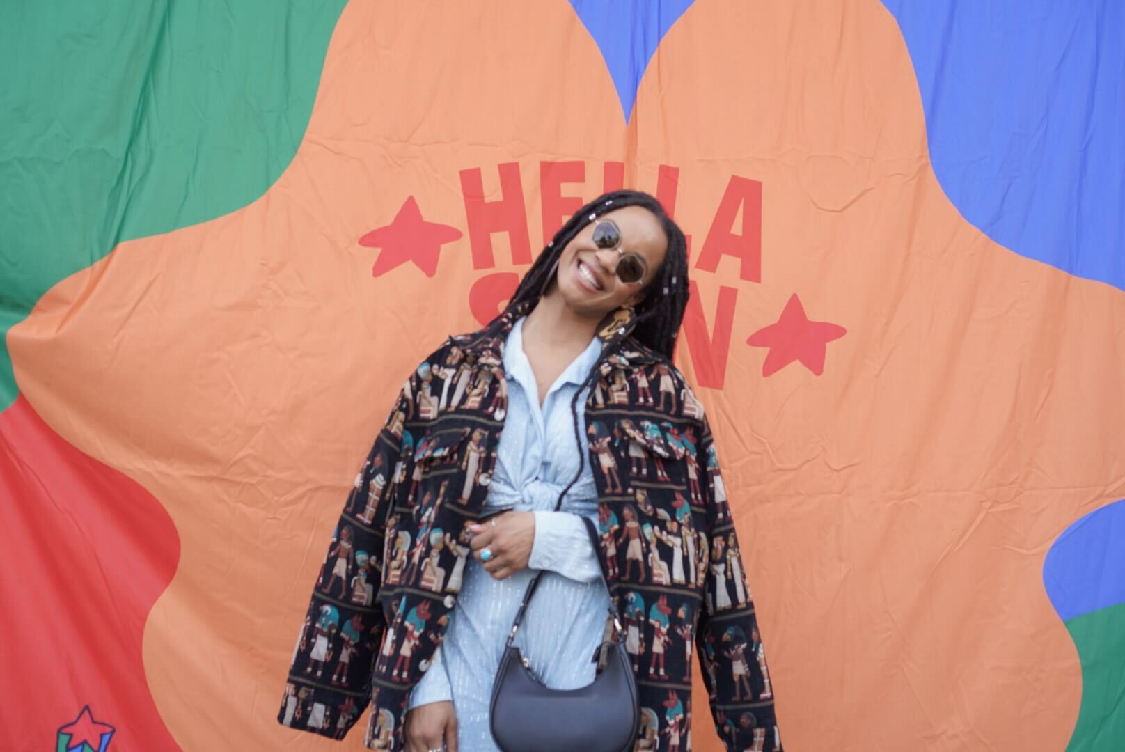 A Black woman with braids poses in front of a colorful background.