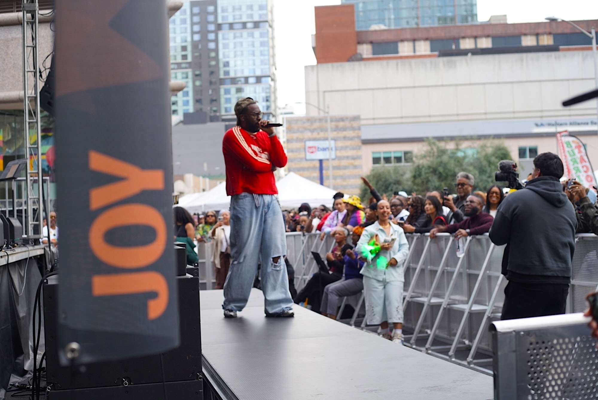The word "joy" is written on a banner in the foreground, as a person stands on stage in the background holding a microphone.