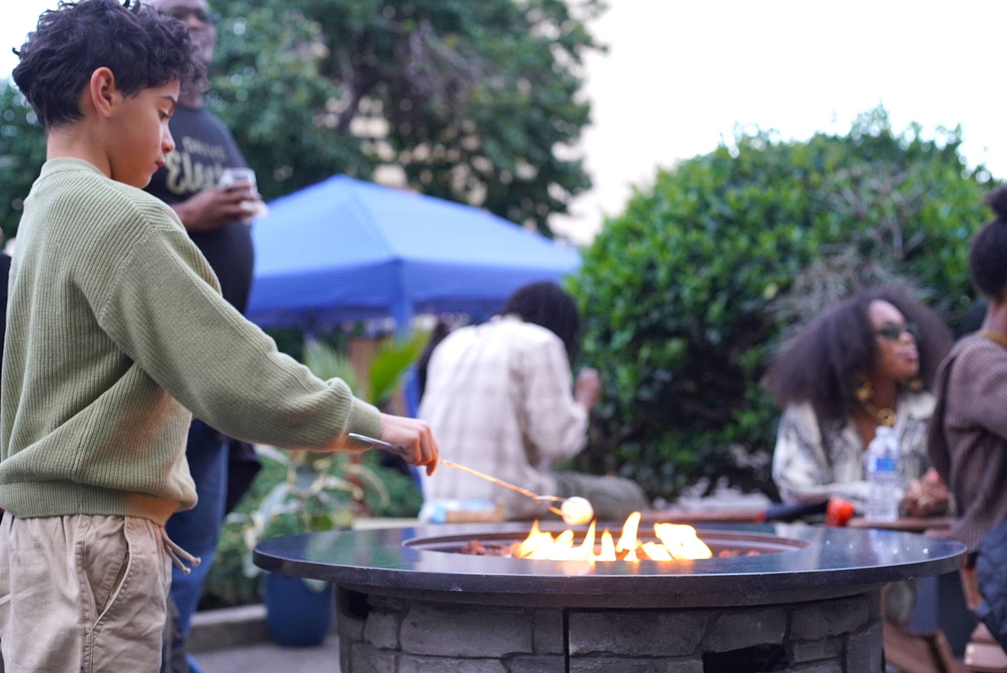 A child in an olive green shirt roasting a marshmallow. 