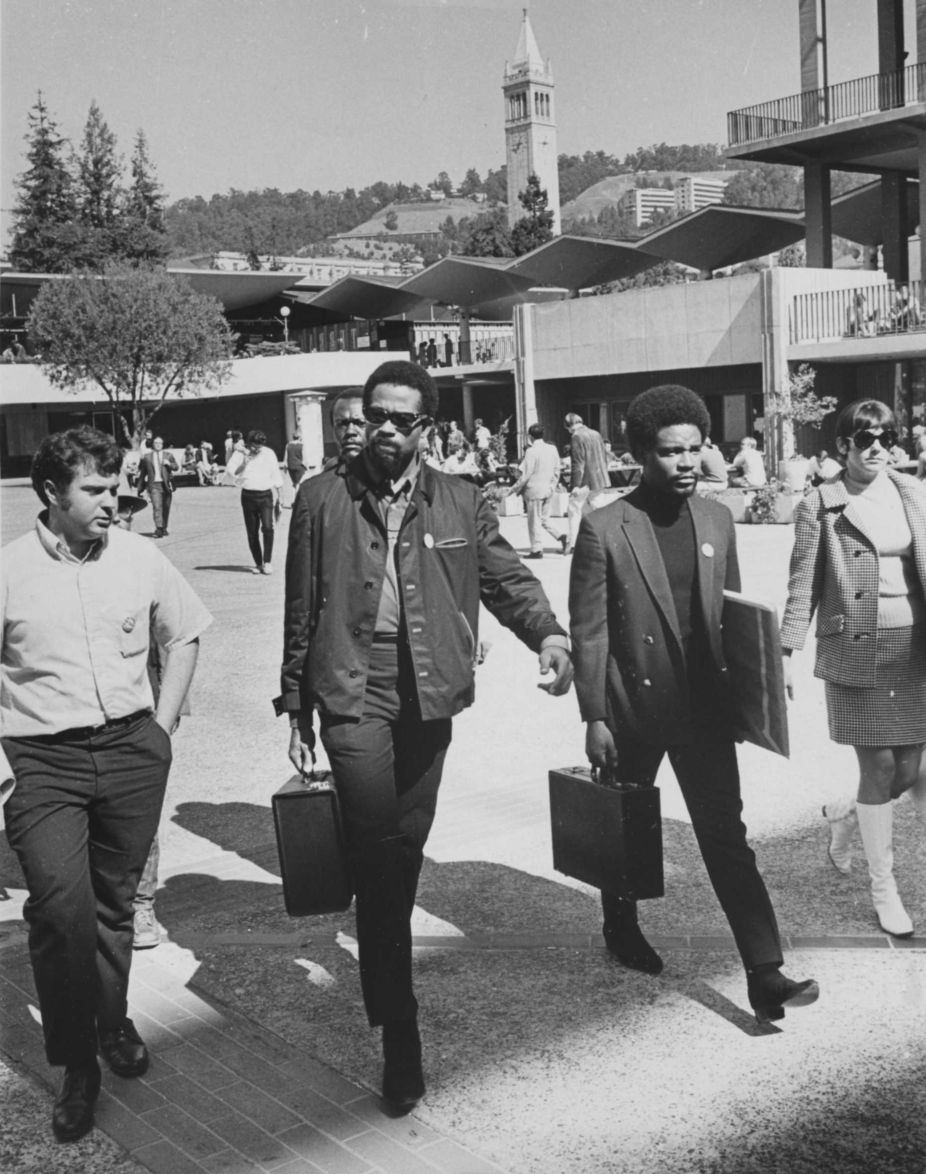 A historical photo of two Black Panthers in leather jackets, one holding art supplies, walking with two white student activists. 