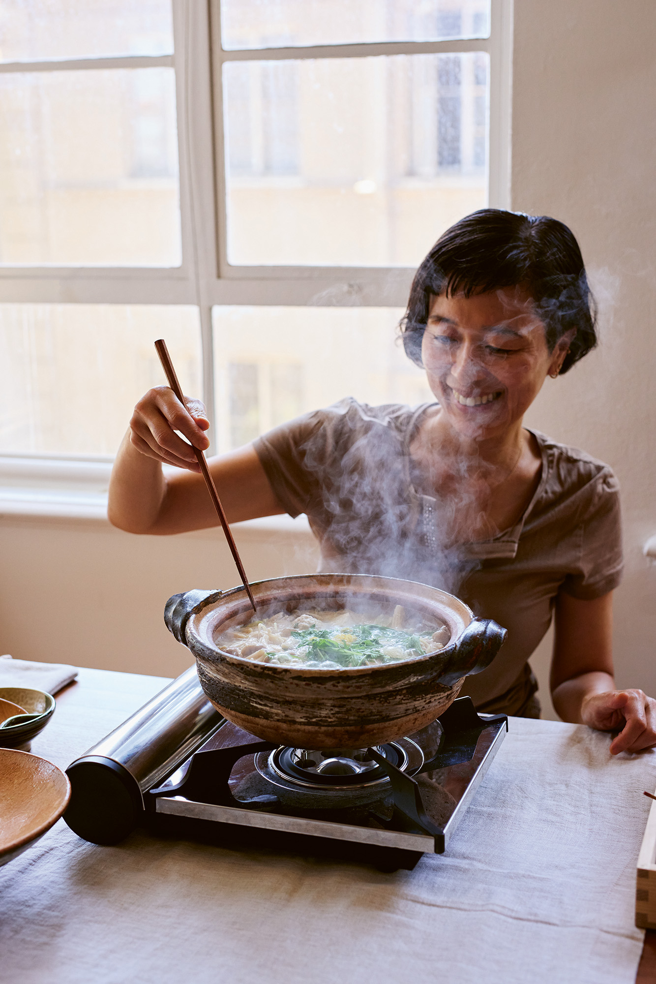 An Asian woman stirs a pot of soup.