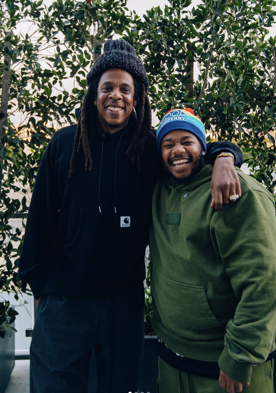 Two men stand next to each other outside, wearing heavy jackets and hats, while posing for a photo.