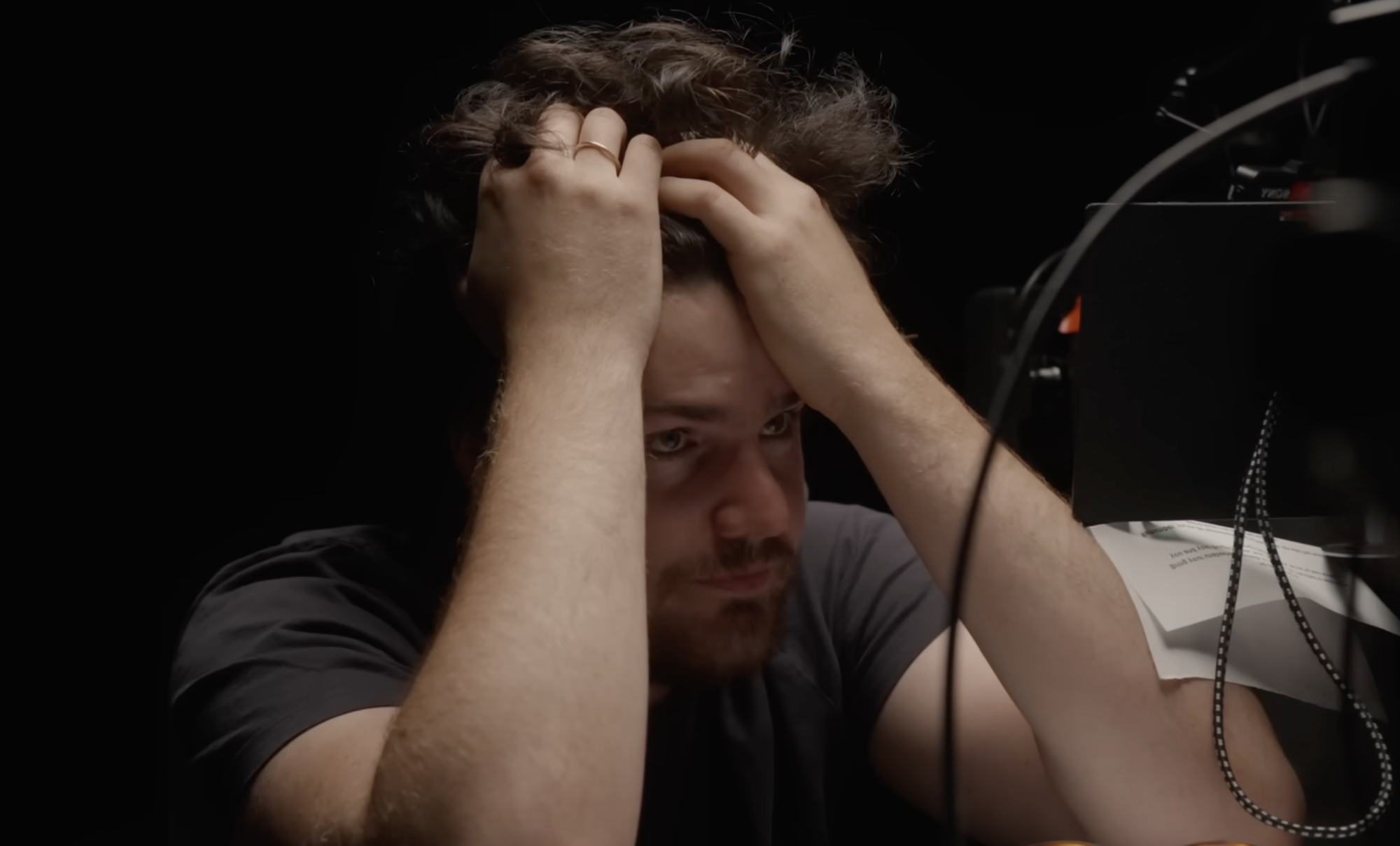A middle aged white man clutches handfuls of his own hair, elbows resting on a desk in front of him, with a stressed facial expression.