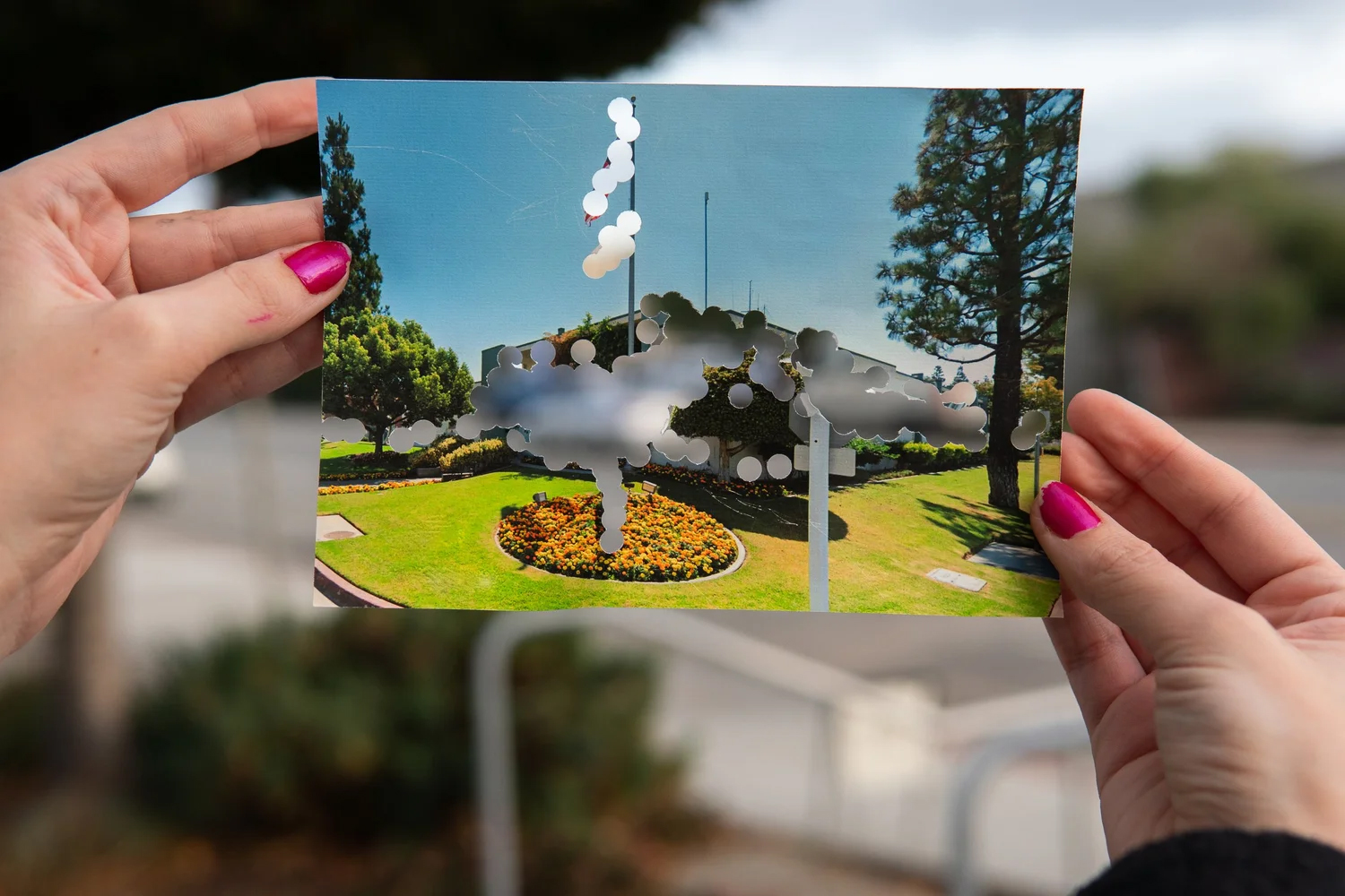two hands hold photo with holes punched through flag and building