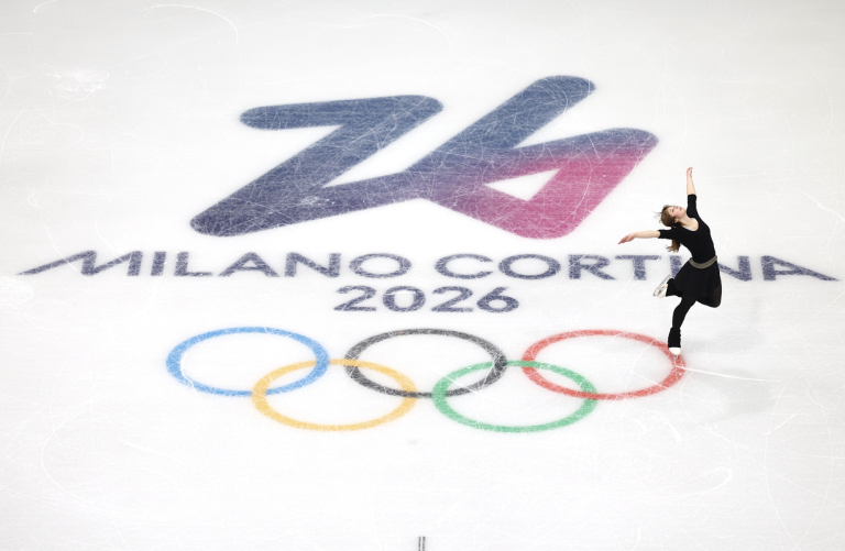 An iceskater in black strikes a pose at the edge of olympic rings depicted on the ice.