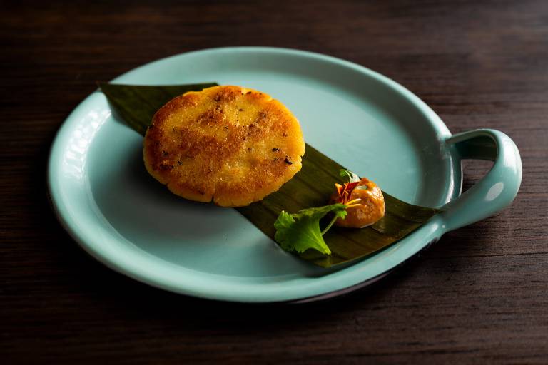 Beautifully plated arepa, served on top of a banana leaf with a delicate dollop of orange sauce.