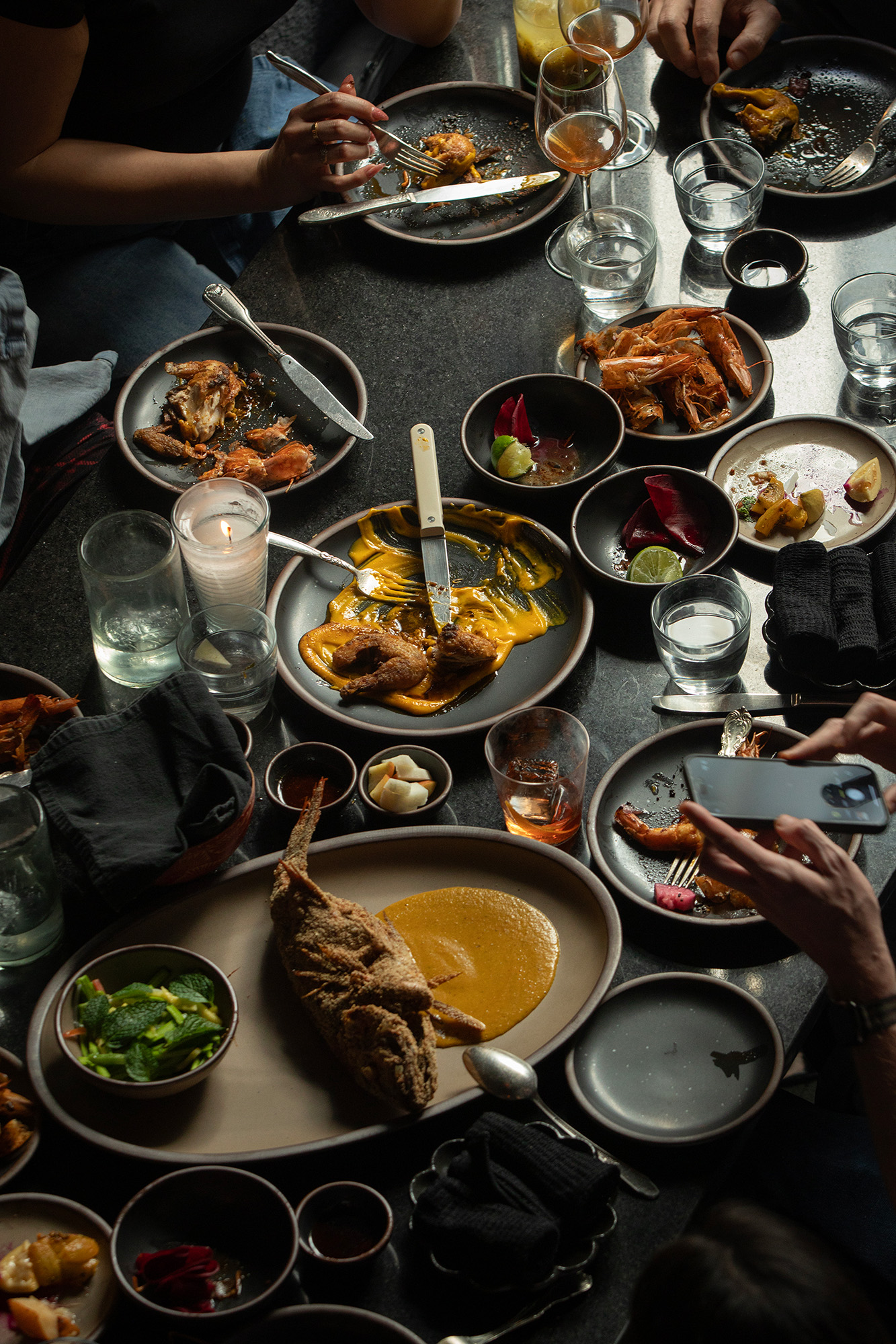 A spread of dishes on a black tabletop &mdash; included is a fried whole fish, head-on shrimp, and salad.