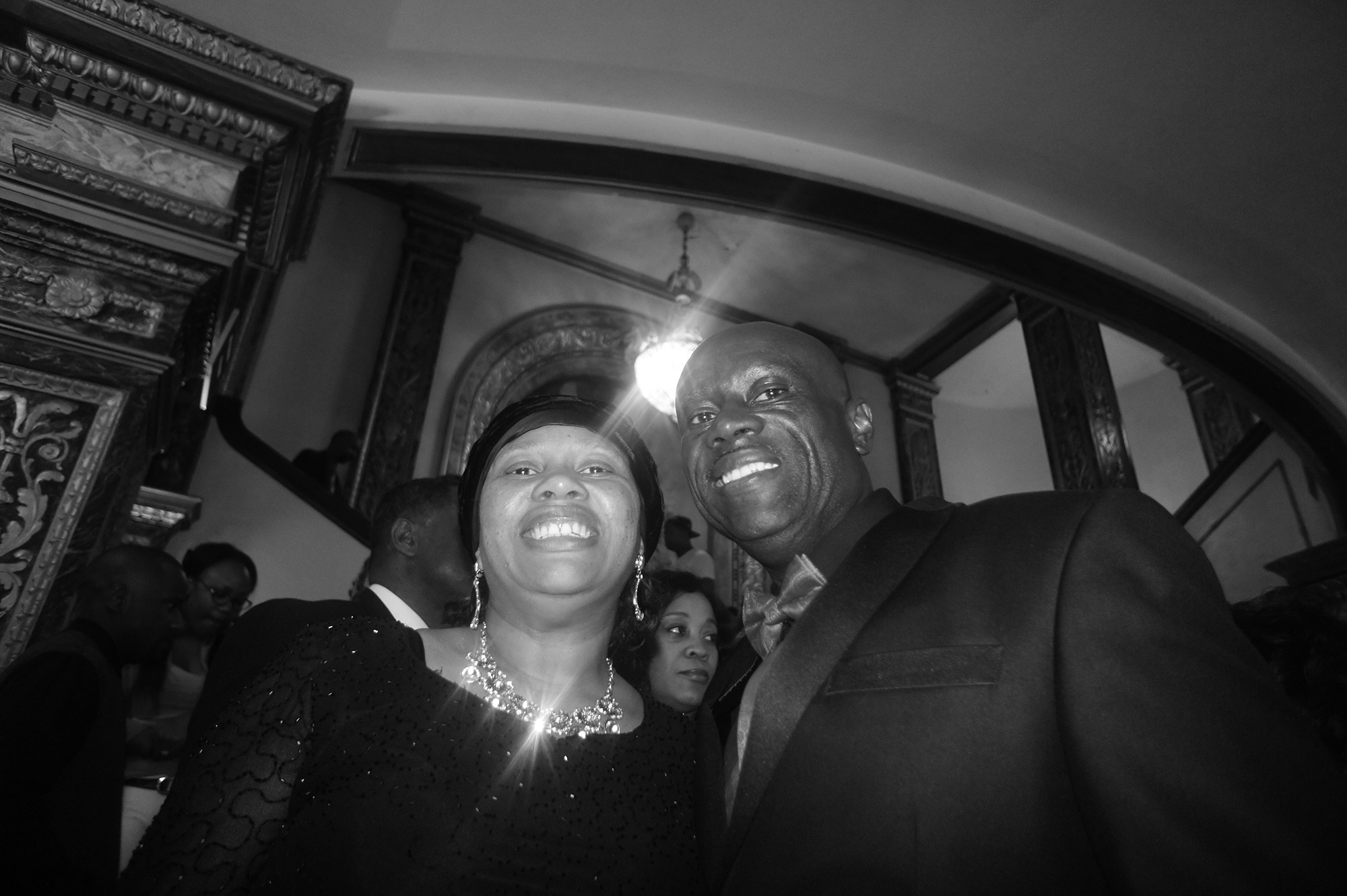 A black and white photo of a woman and a man posing while wearing dress attire.