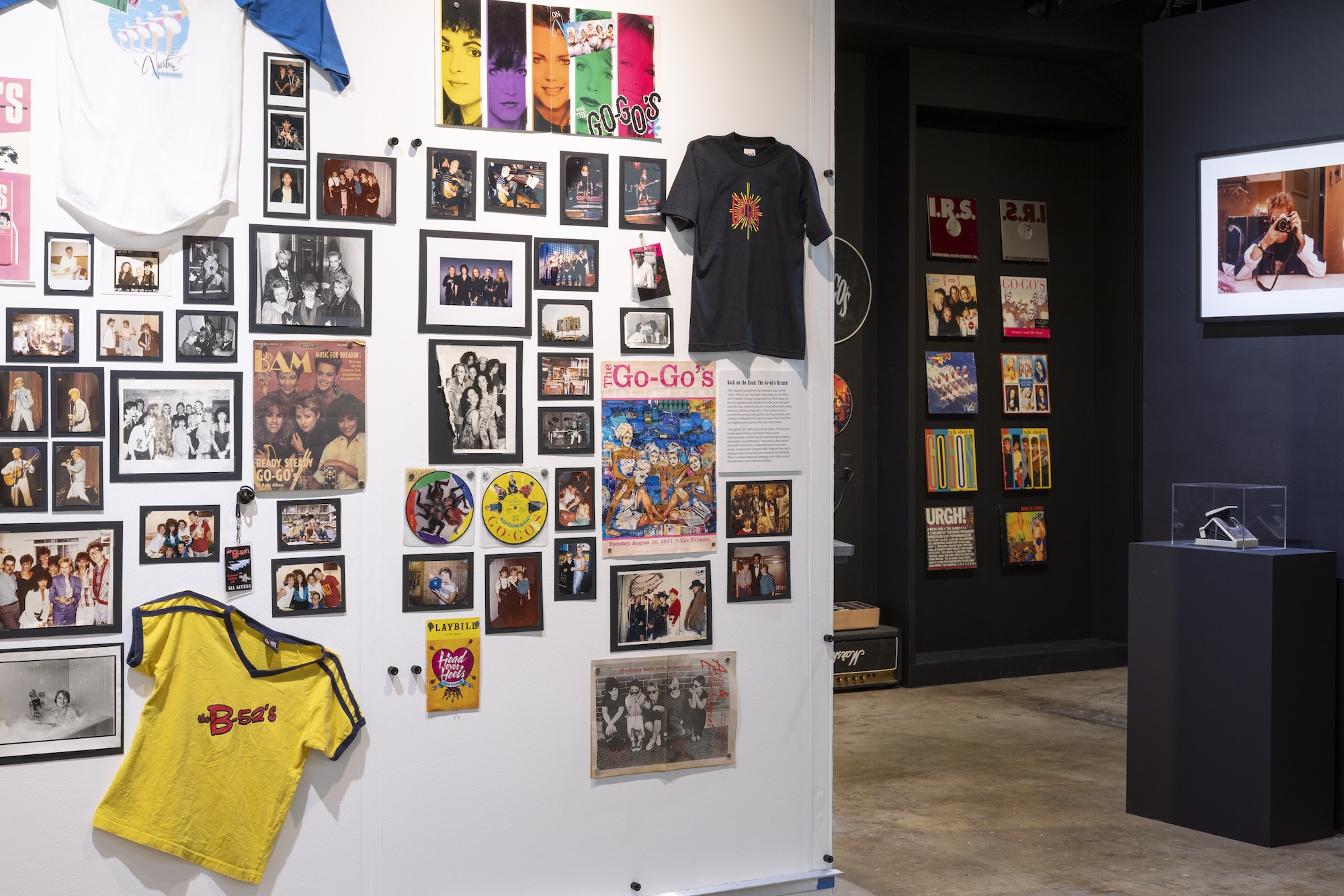 A gallery wall covered in photos, posters, t-shirts and other ephemera, all about The Go-Go&rsquo;s.