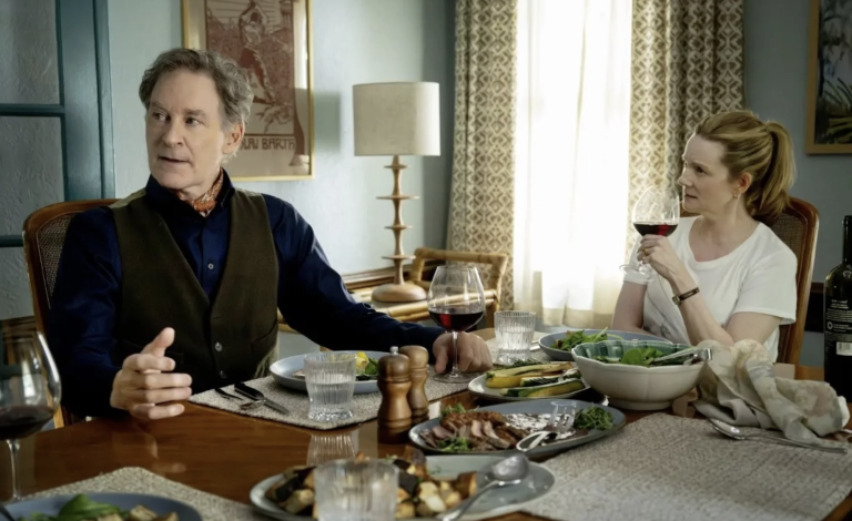 A white man and white woman sit at a family dinner table. He is talking, she is drinking red wine.