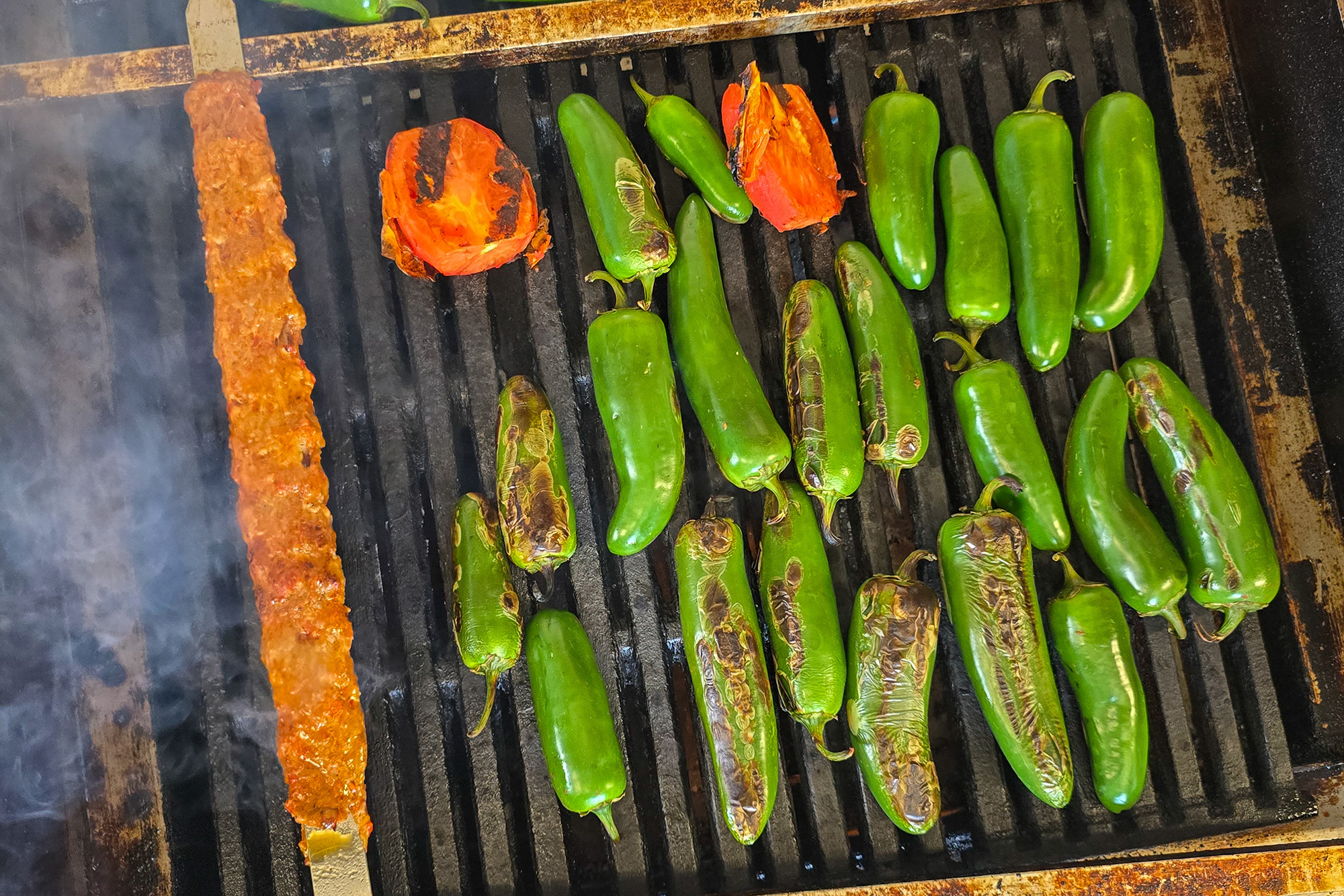 Jalape&ntilde;os, tomatoes and Adana kebab on a hot grill.