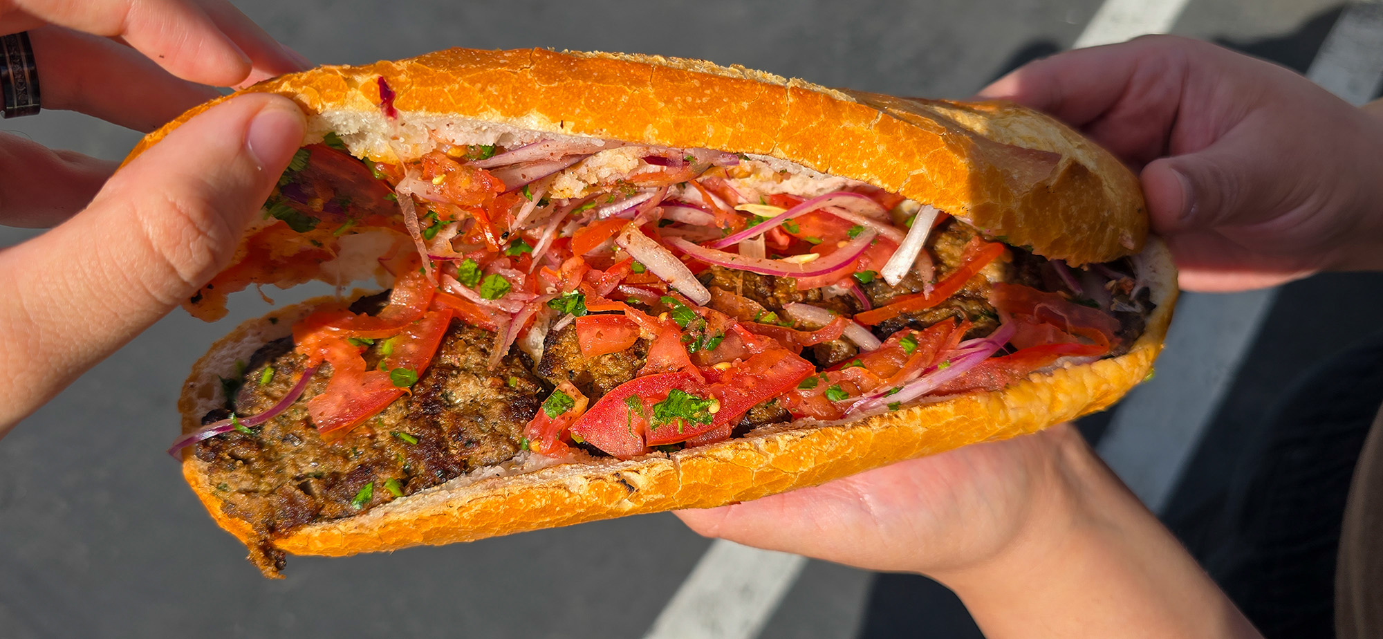 A kofte keba sandwich, opened to show the meat, tomatoes, and onions inside.