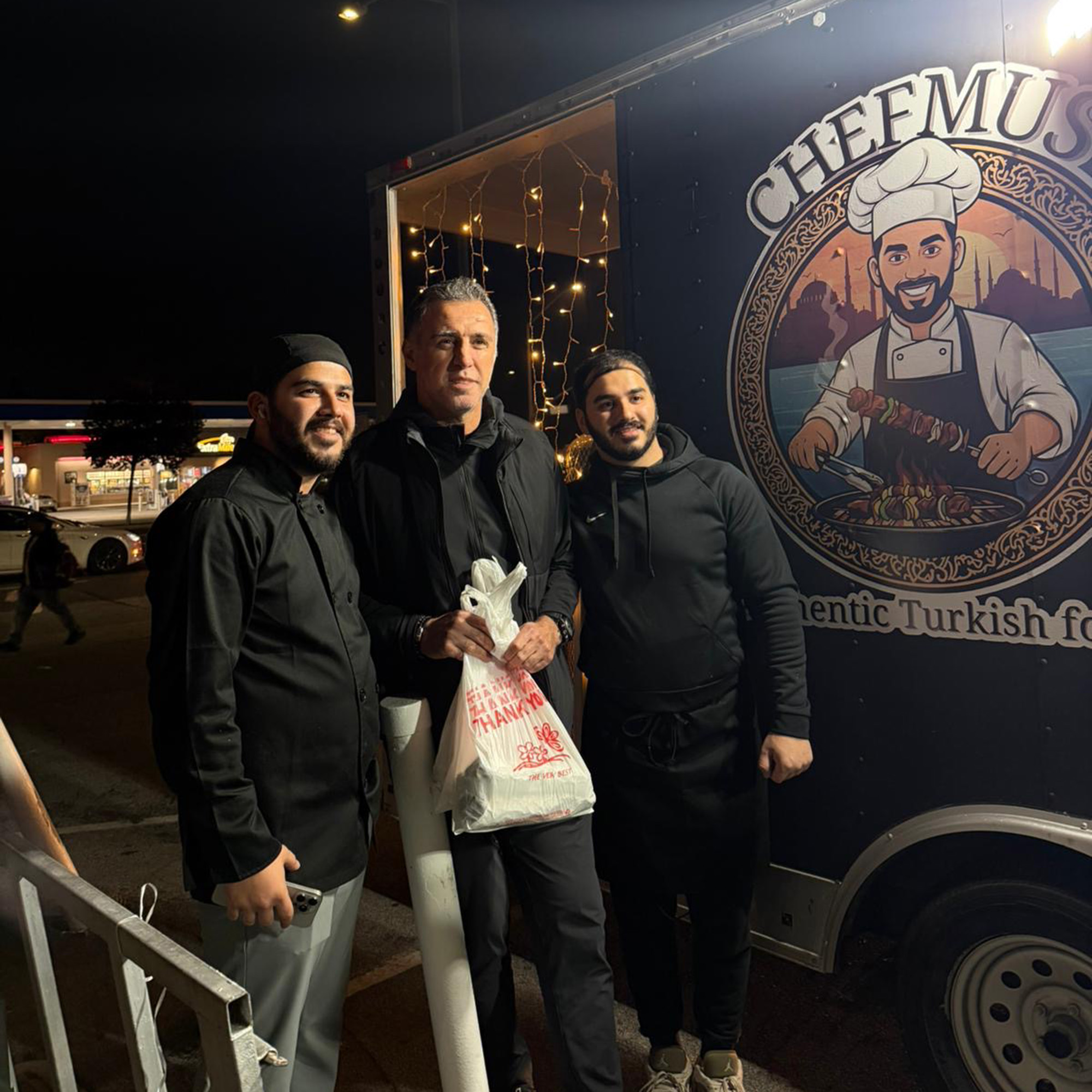 Three men pose for a photo next to a food truck. Text on the truck reads, "Chefmus."