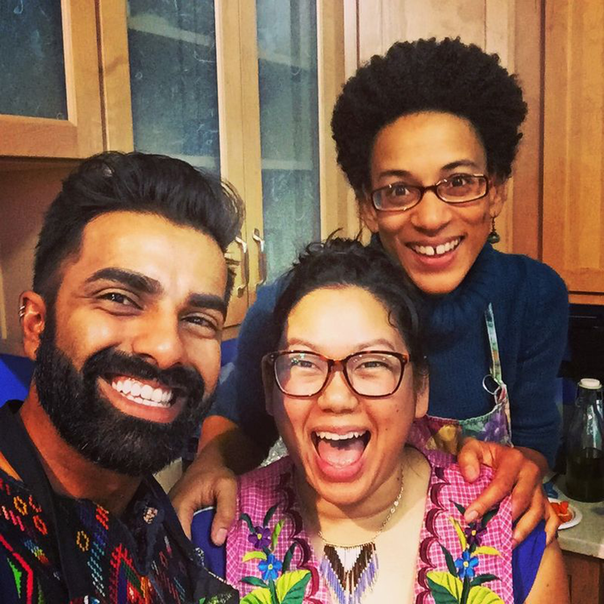 Three smiling people posing for a portrait in front of some kitchen cabinets