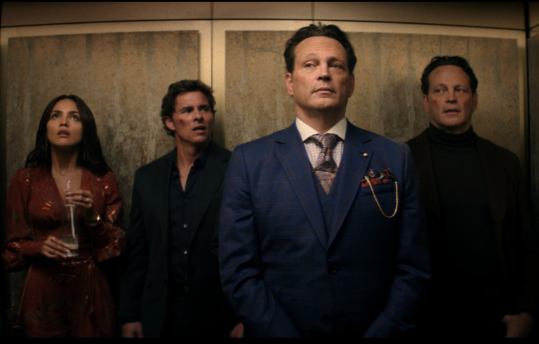 An attractive woman, a confused looking man and two identical, dapper men stand in an elevator side by side.