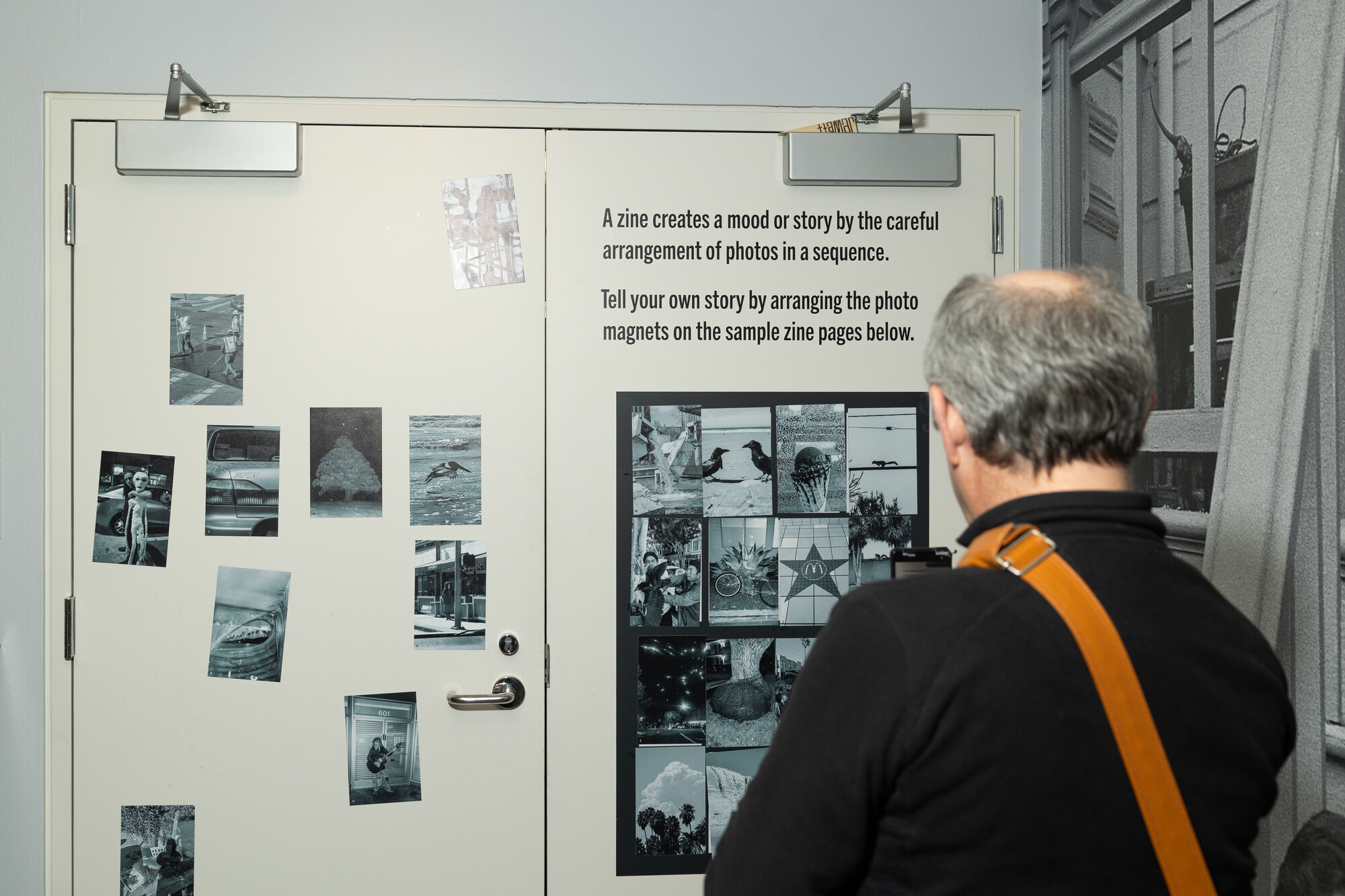 A white man with receding hairline examines a wall covered with black and white photo magnets, arranged on a white door. 