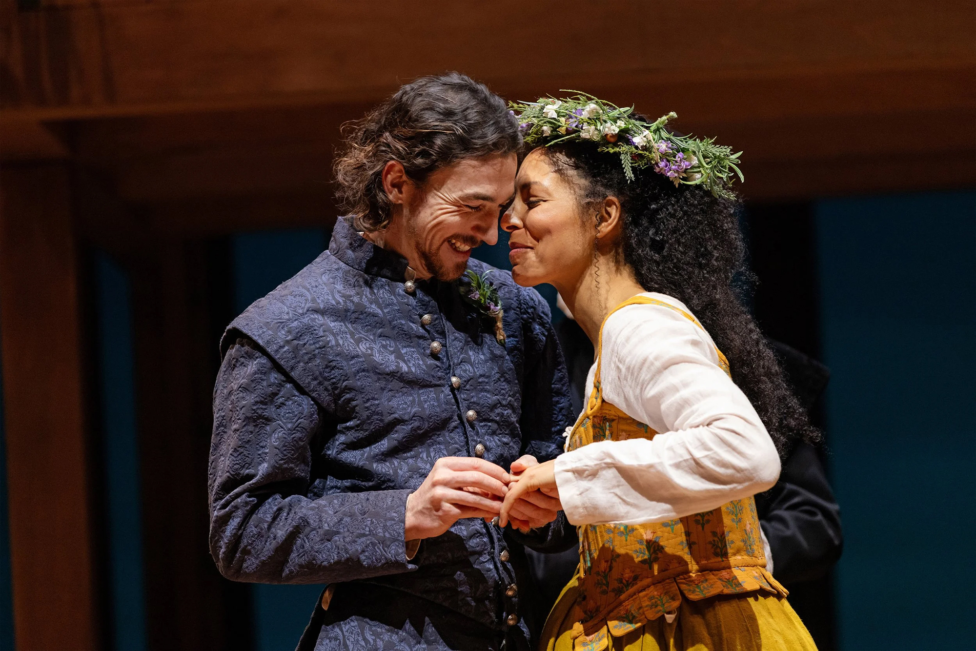 A man in blue and a woman with a flower crown nuzzle up against one another