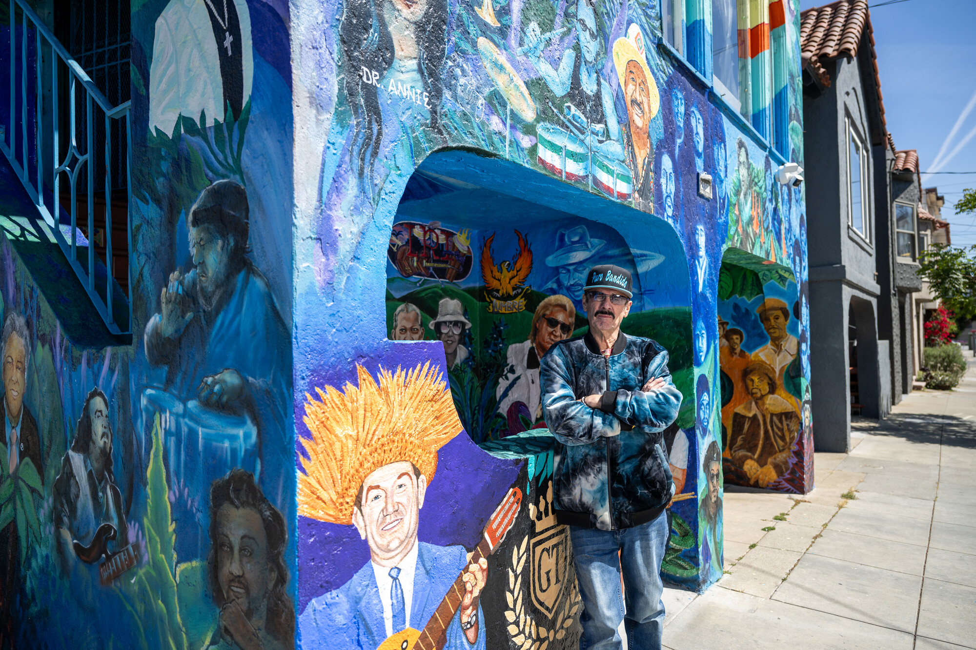 man with arms crossed in front of mural covered home