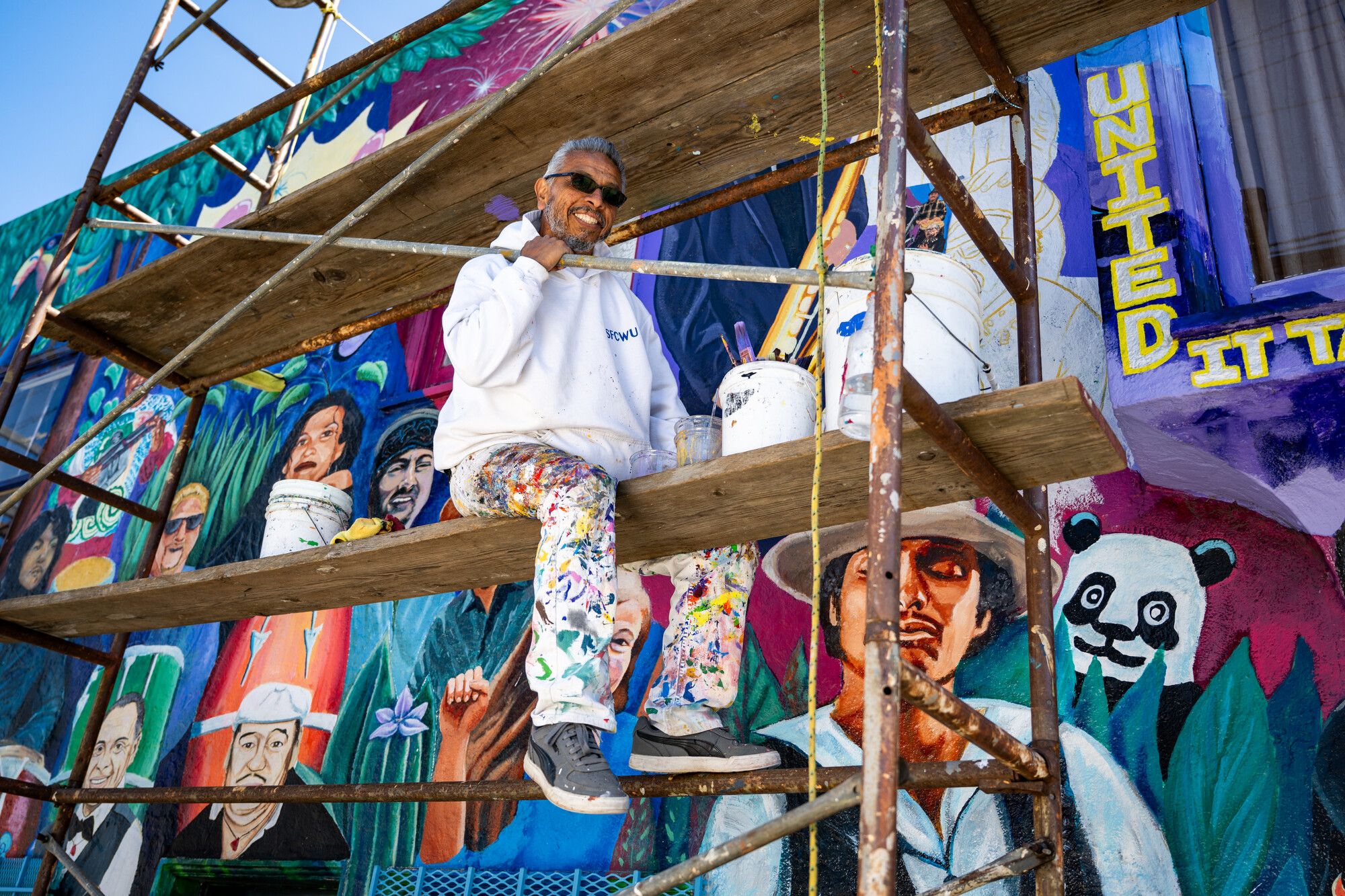 smiling man on scaffolding in front of colorful mural
