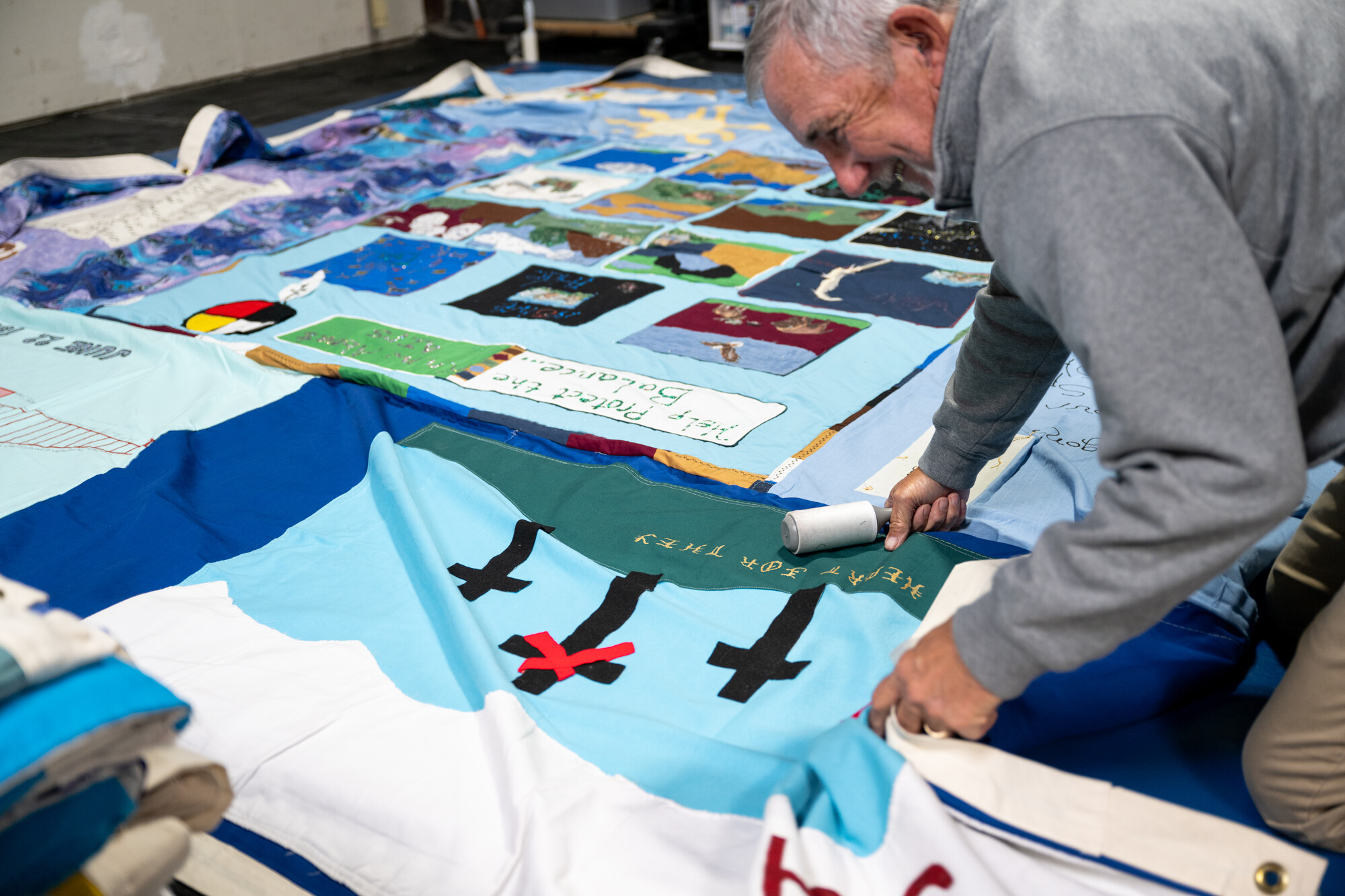 older white man kneels beside quilt with lint roller
