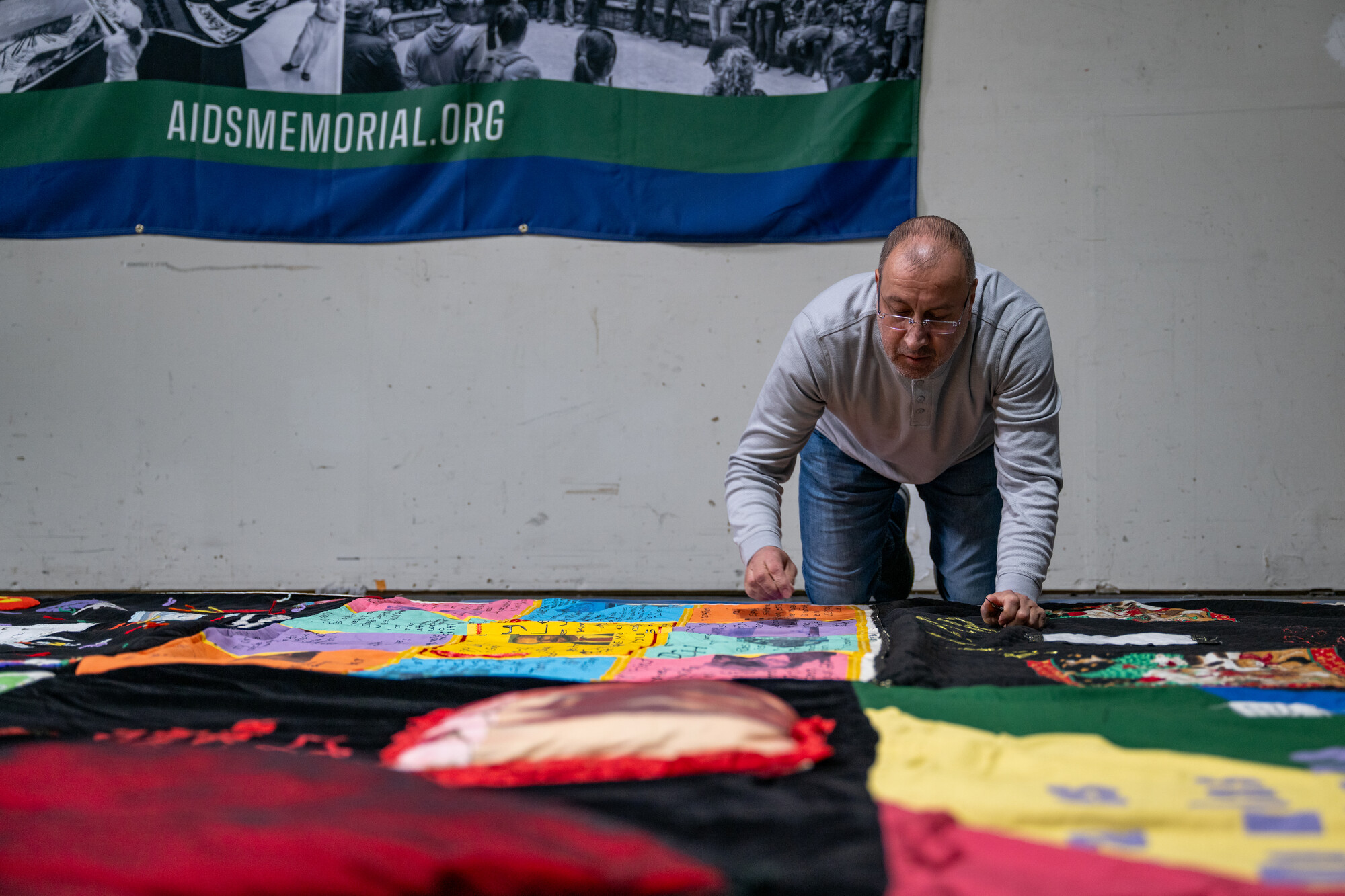 older white man kneels and reaches across quilt
