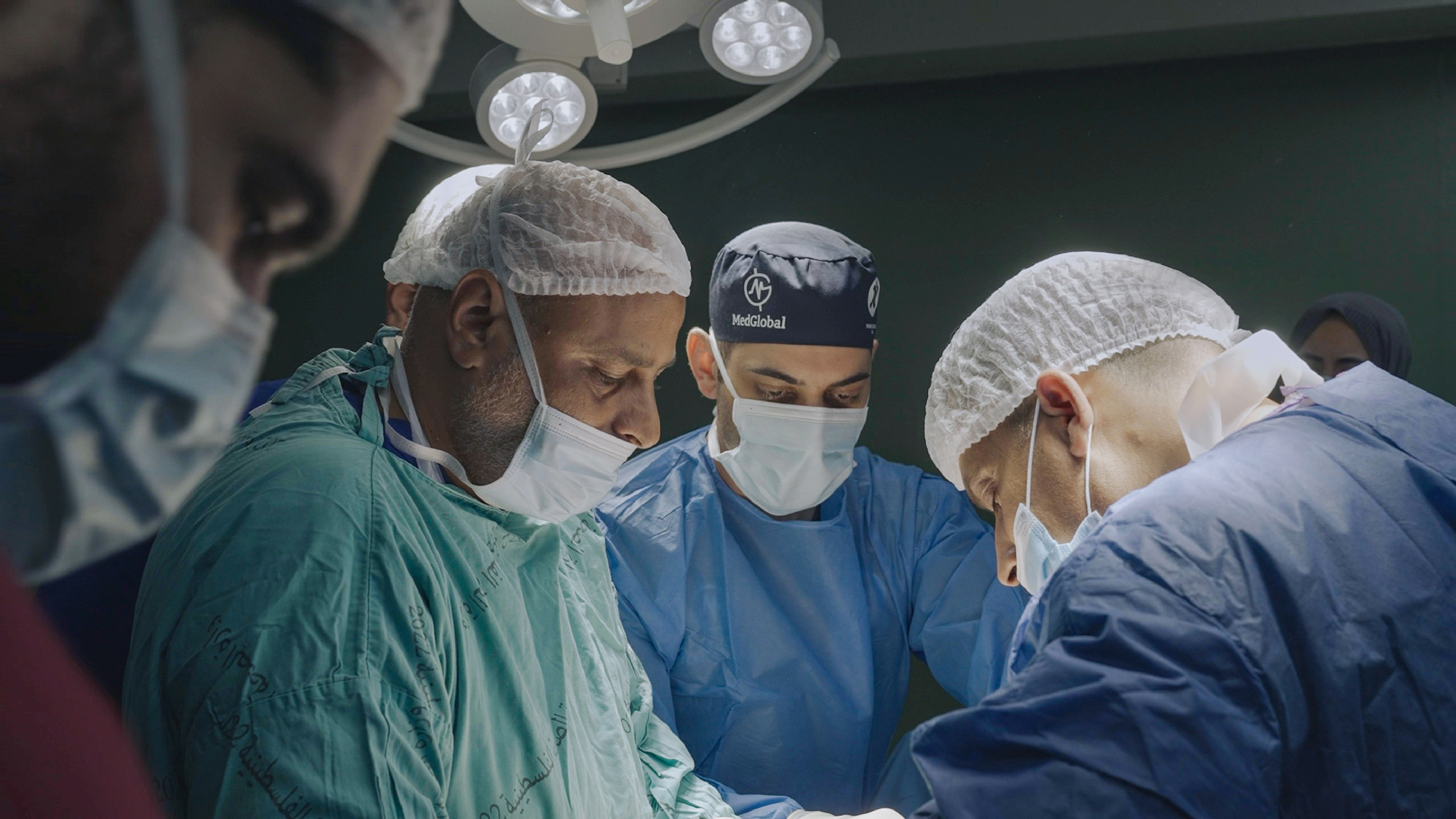 four people in scrubs look down in operating room