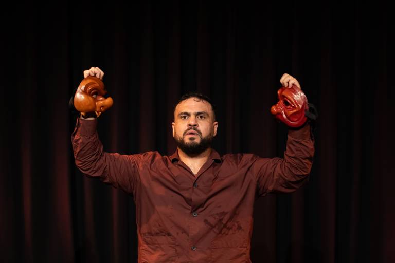 man holds two halves of mask on dark stage