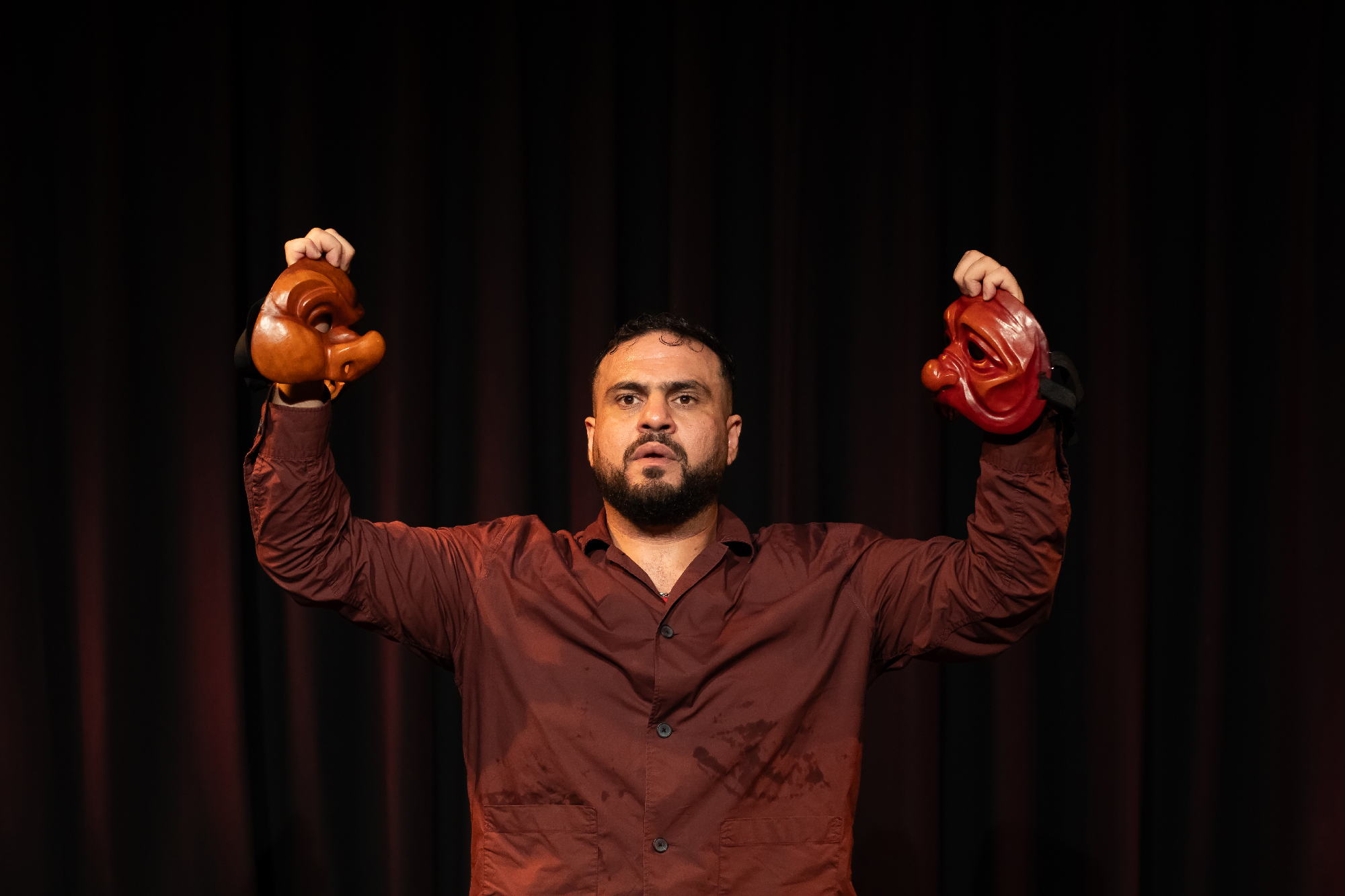 man holds two halves of mask on dark stage