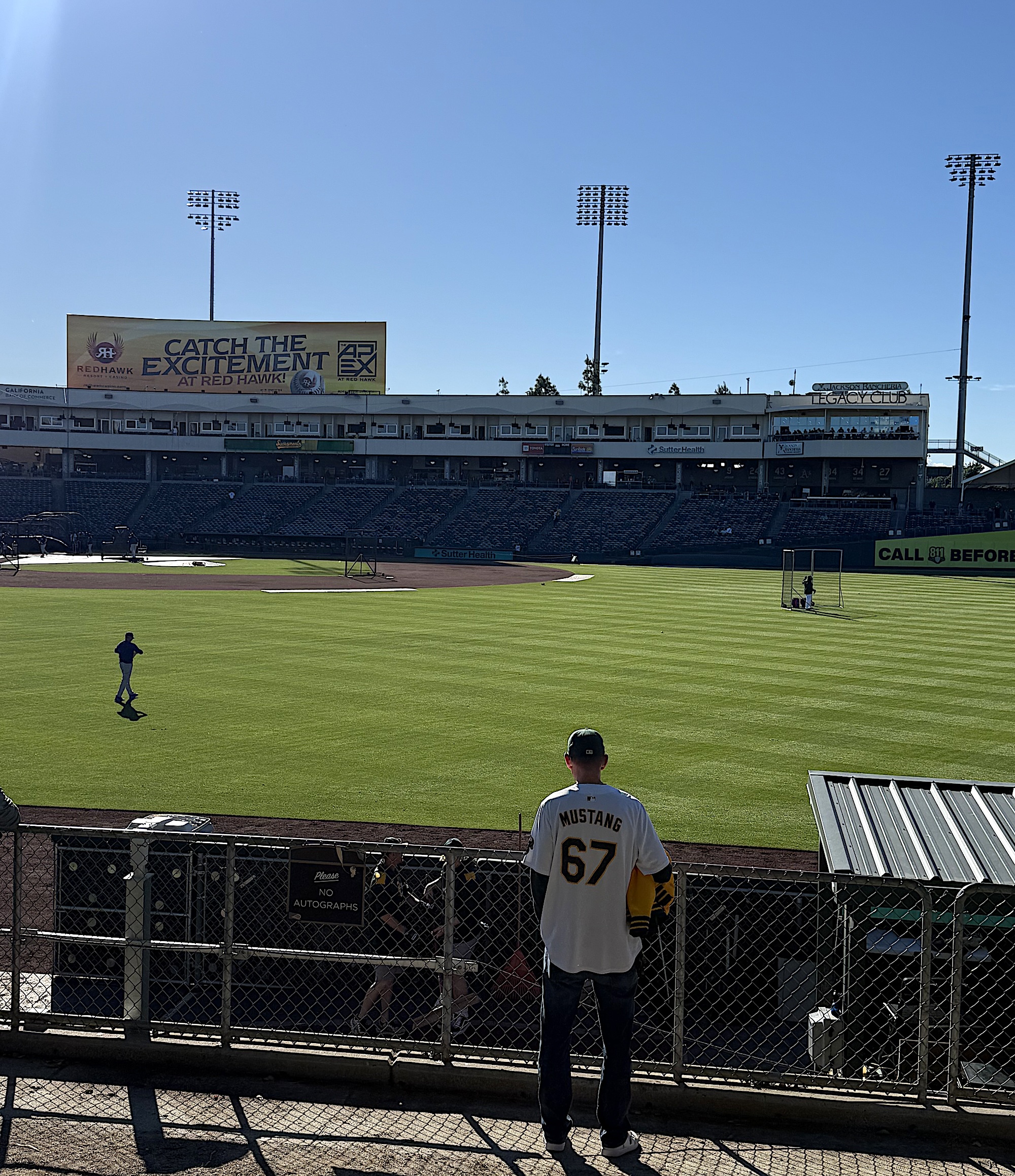 The backside of a fan standing in the outfield of a baseball stadium.