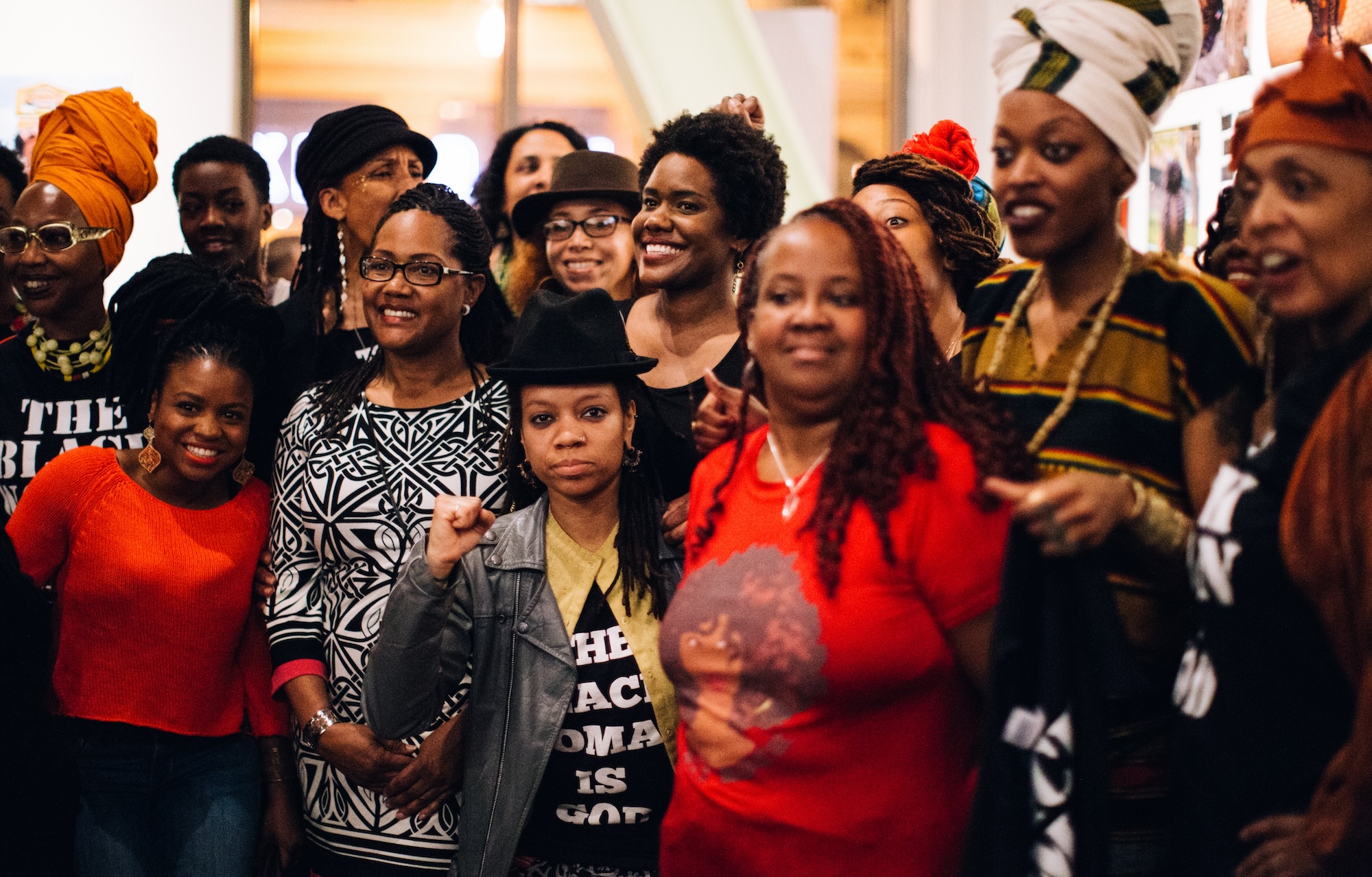 A large gathering of African American women artists pose for a photo inside of a gallery.