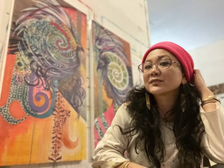 A woman in a red hat sits in front of her art.