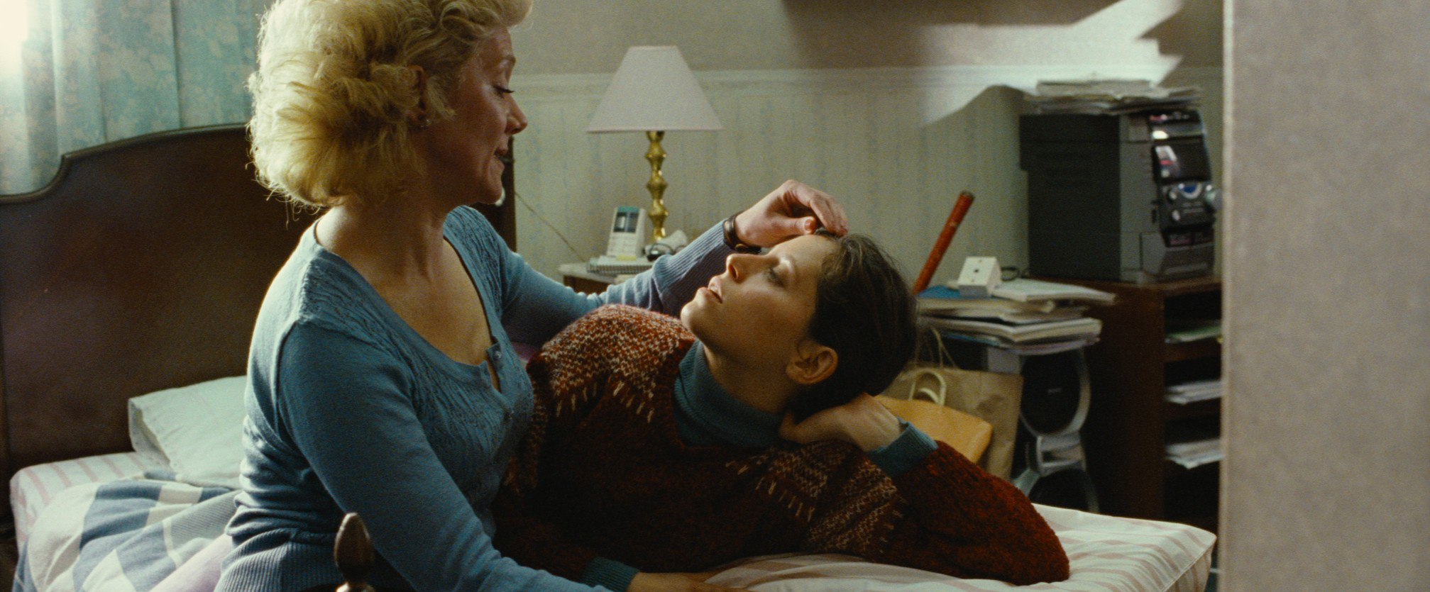 older woman caresses younger woman's face as they sit on bed