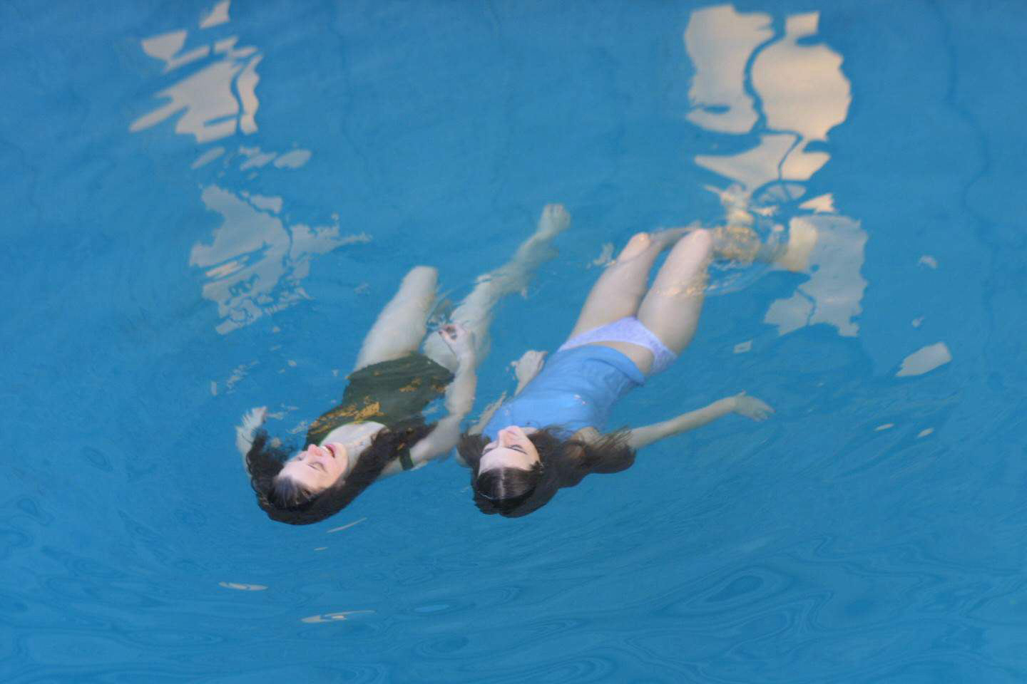 two girls swim on their backs in blue pool