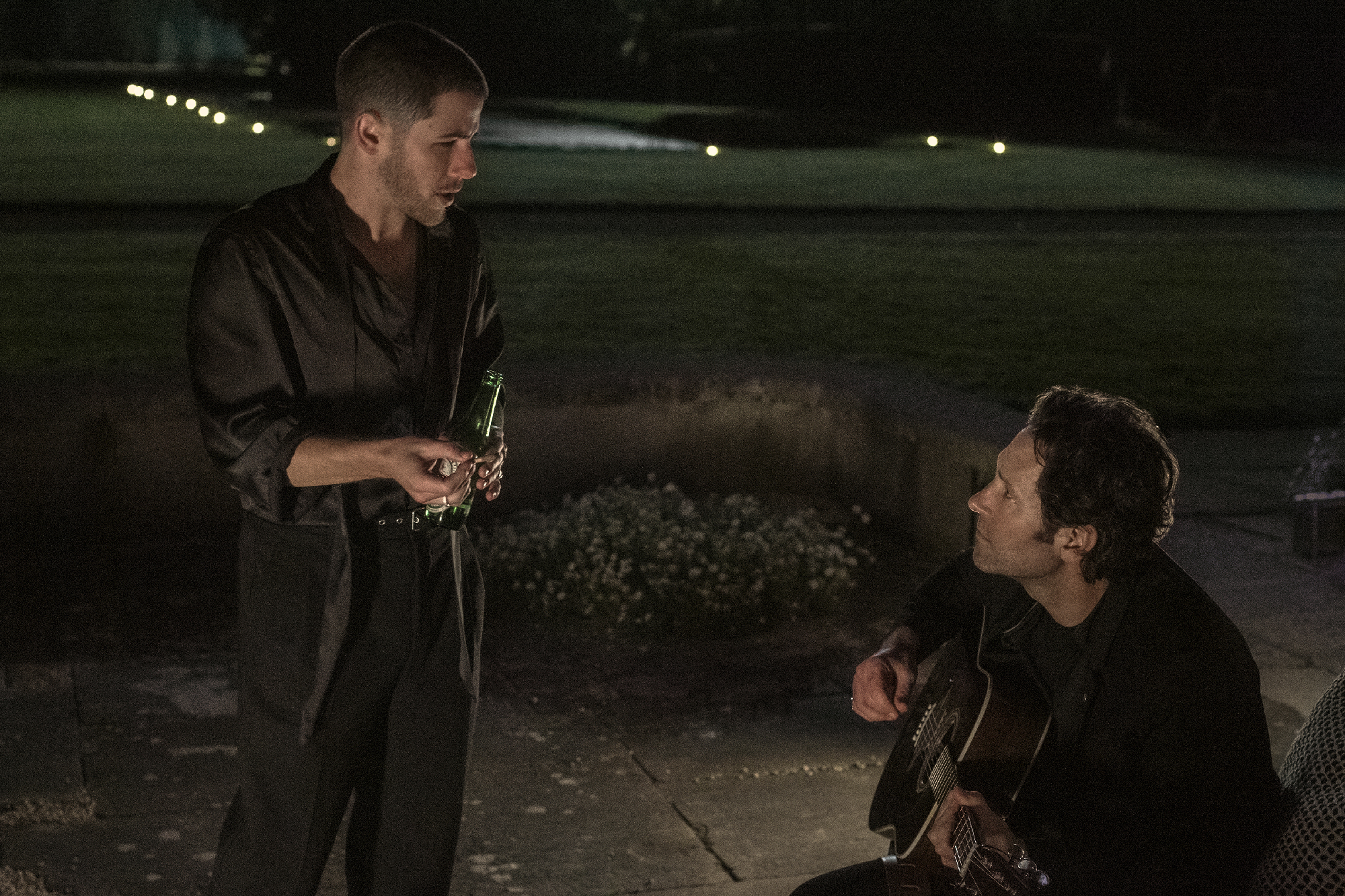 younger man with beer faces middle-aged man with guitar
