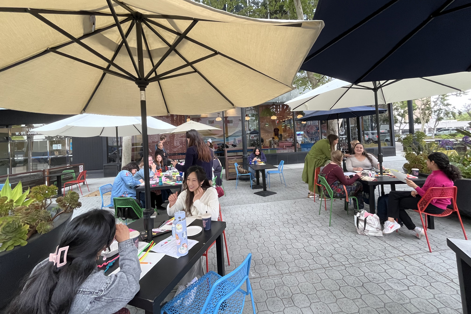 smiling people with art supplies across several outdoor tables at cafe