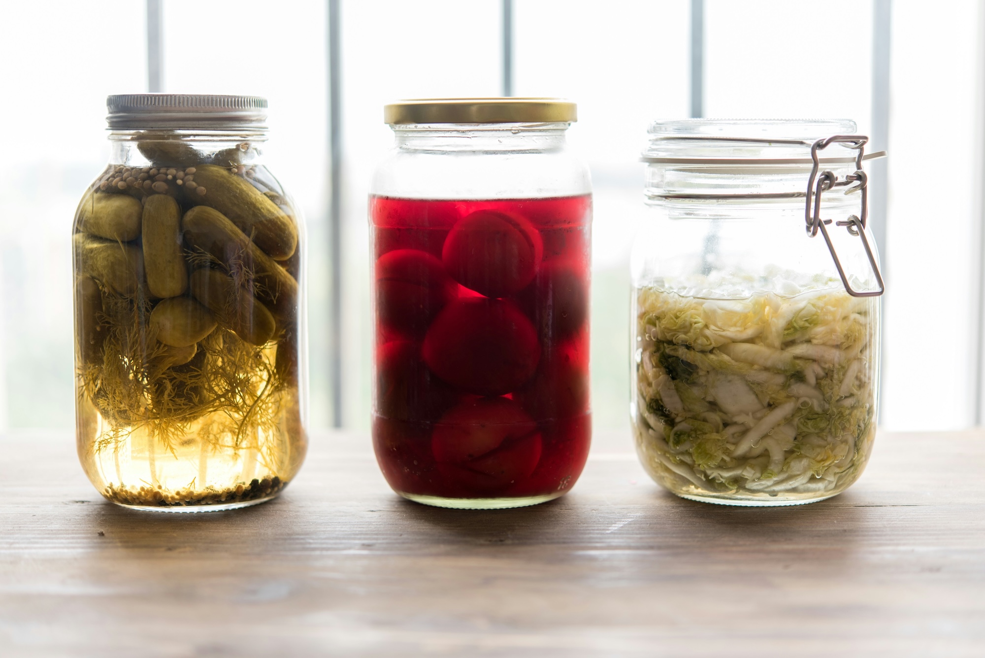 Three sealed jars lined up in a row, containing pickles, onions and cabbage.