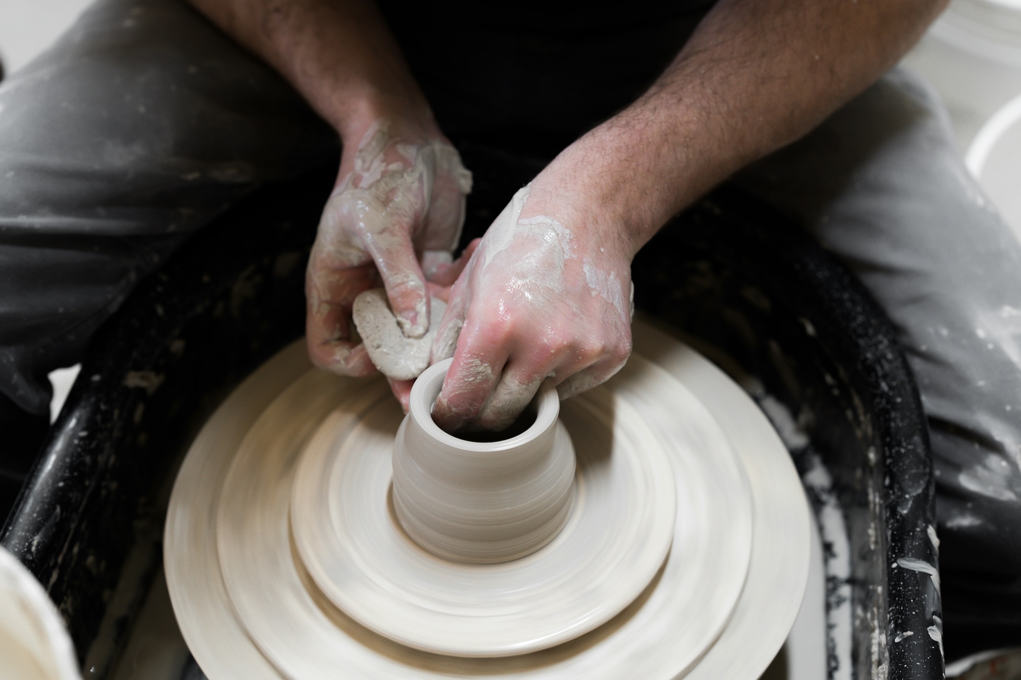A close-up of clay covered hands working a cup on a potters wheel.