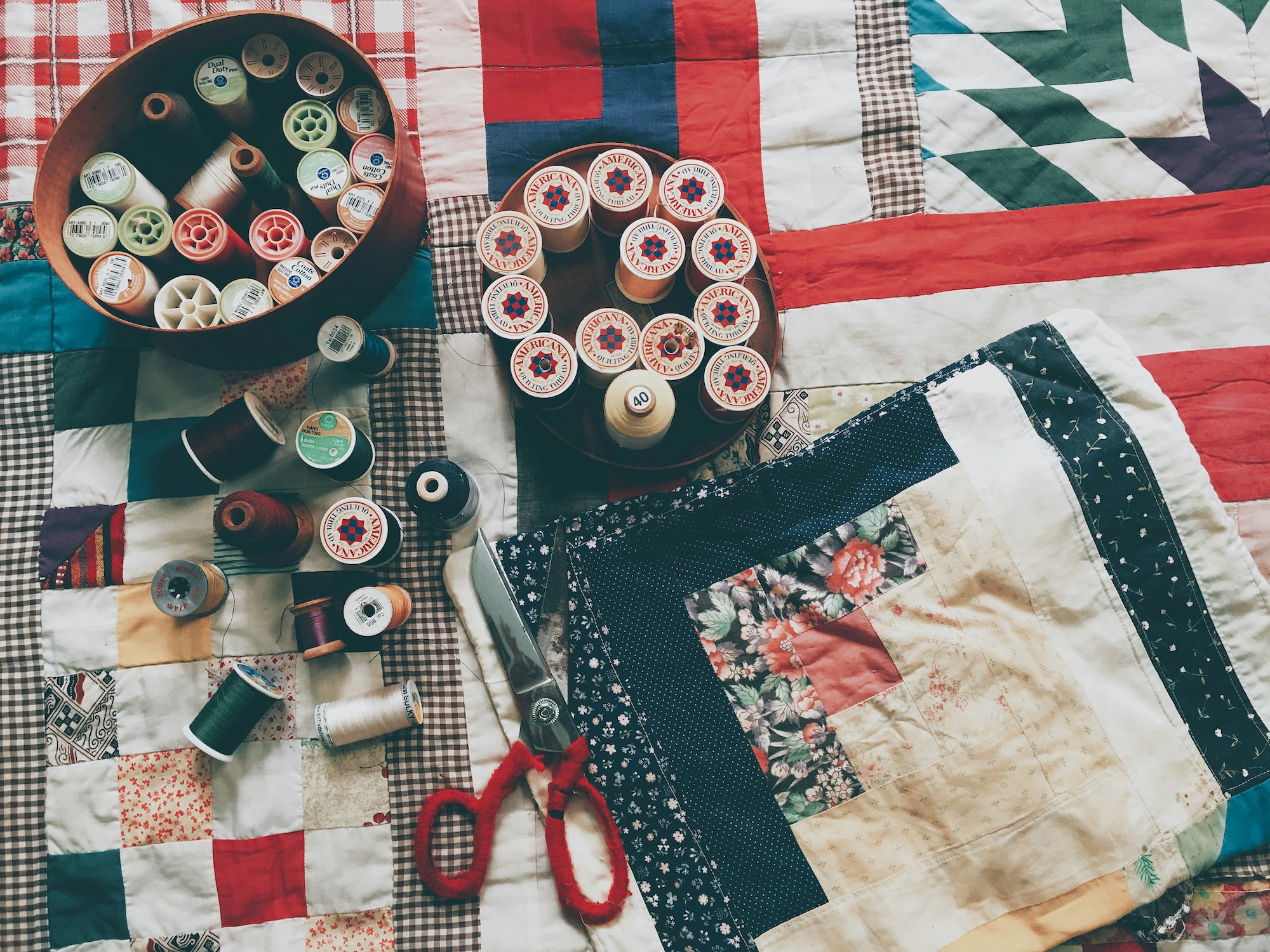 A red, white and blue quilt covered with thread, scissors and other quilting materials.